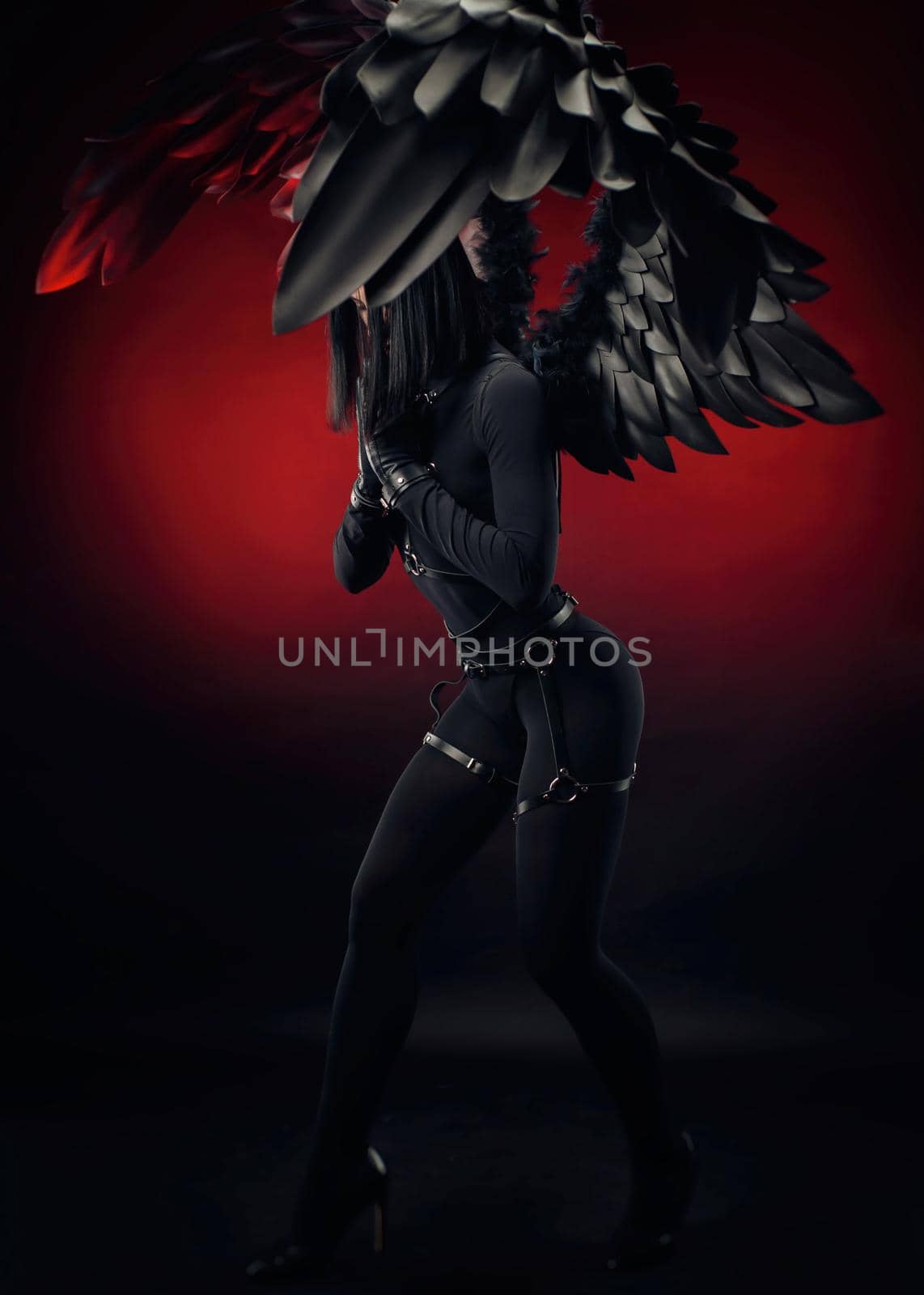 the woman in a black bodysuit with leather straps and black wings on a dark red background