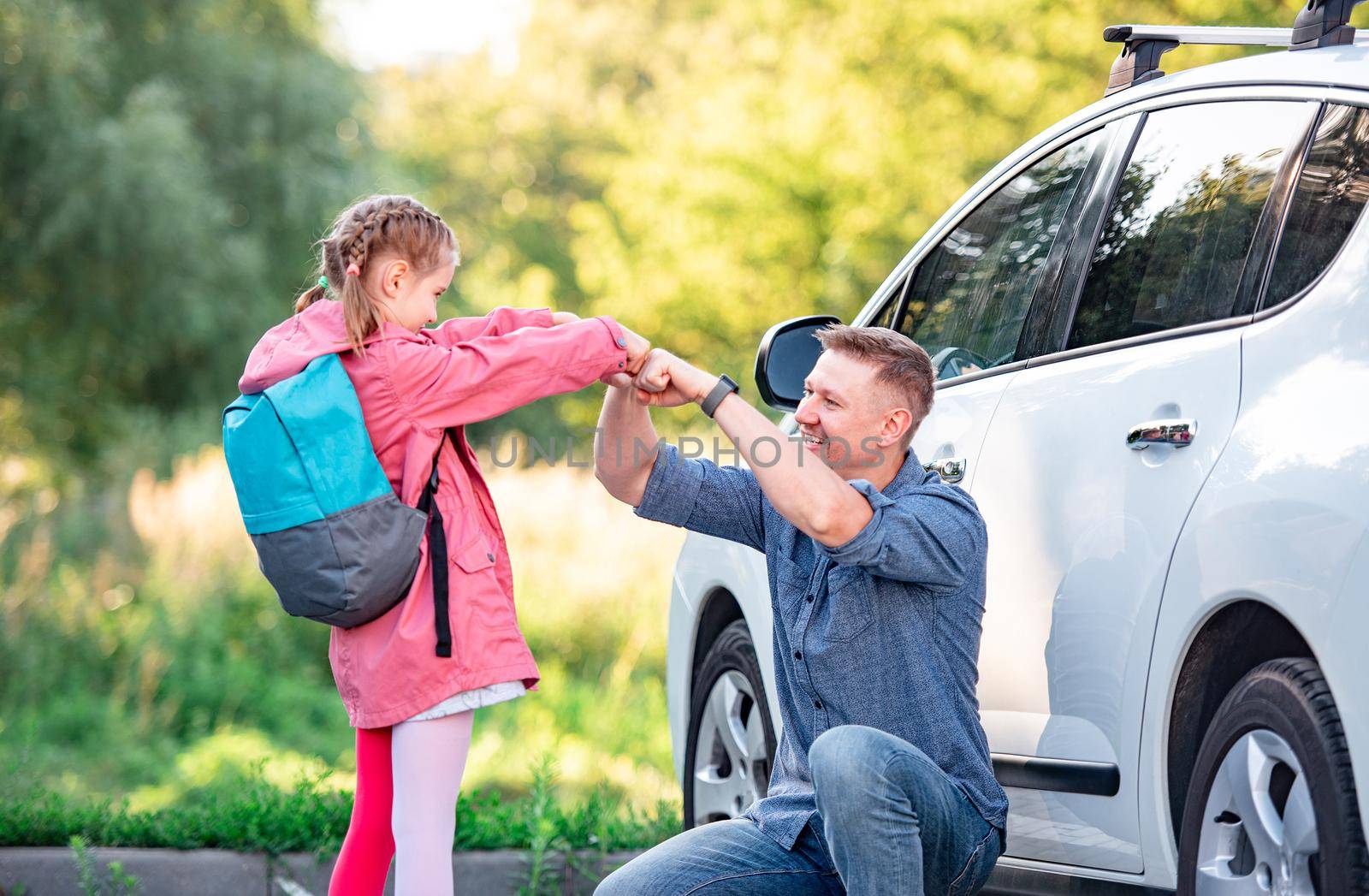 Father banging fists with daughter going back to school outdoors near car