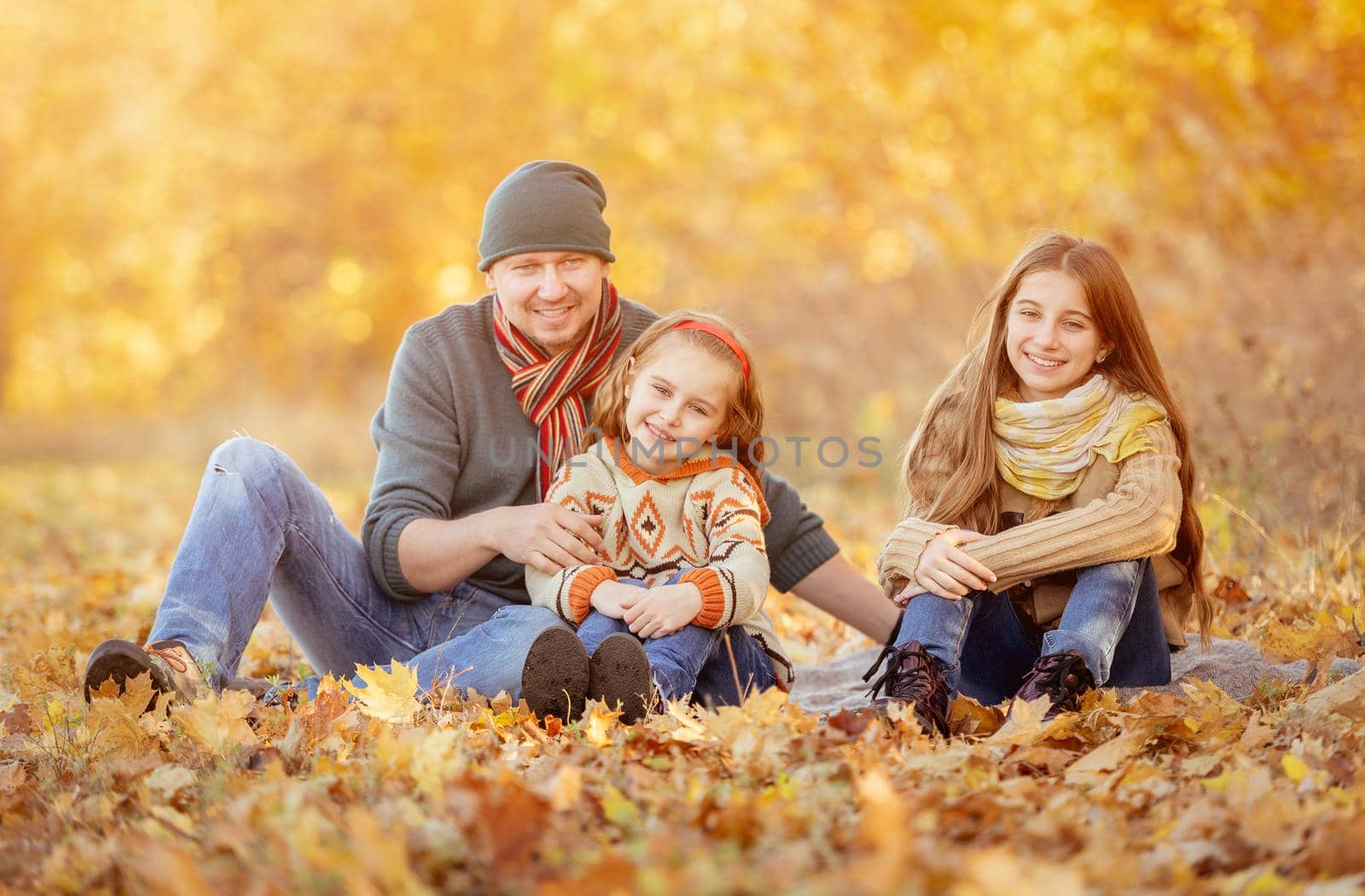 Daughters and father sitting in autumn leaves