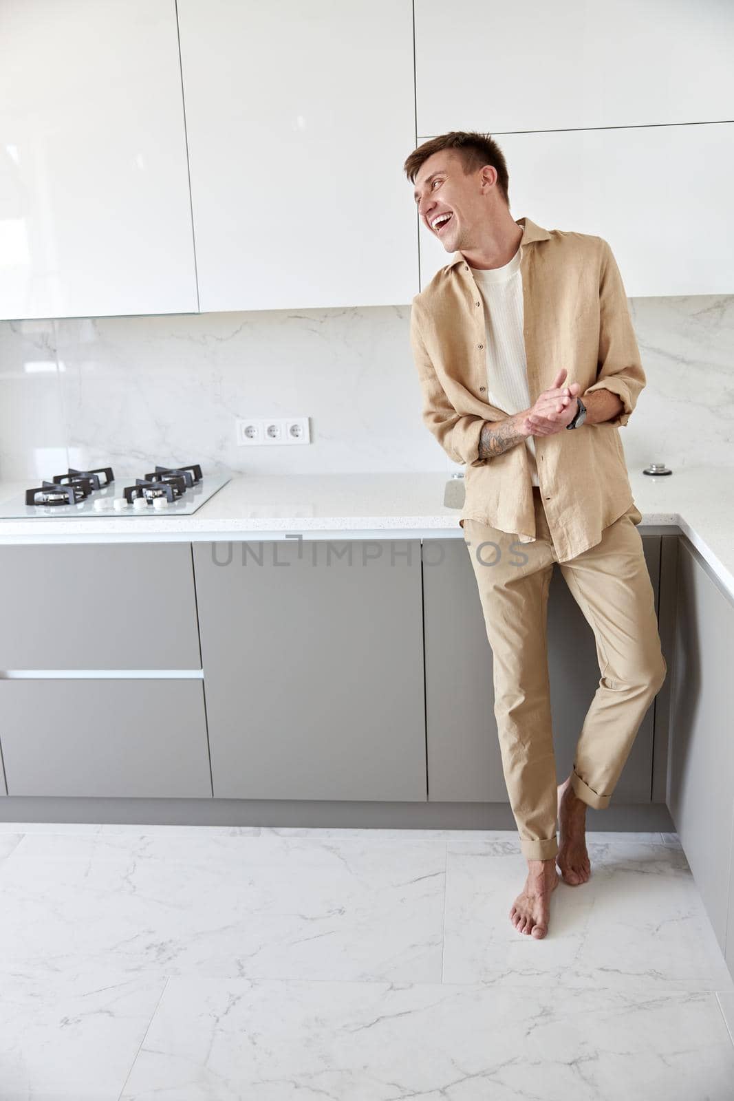 Happy handsome man is standing on minimalistic kitchen and smiling