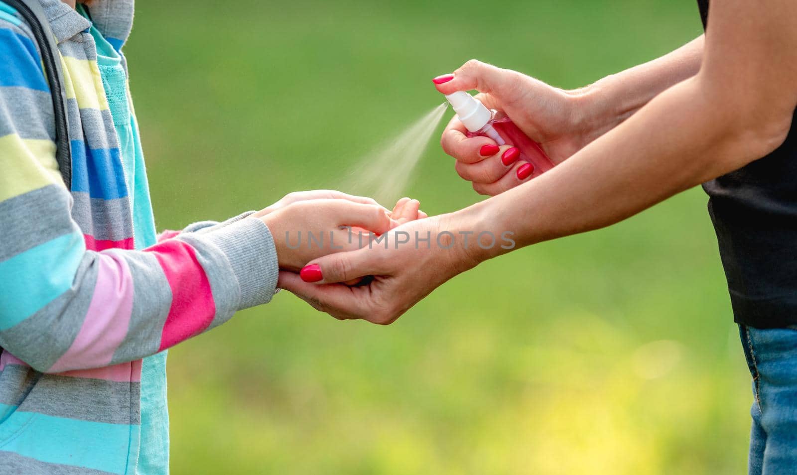 Woman spreading sanitizer on girl hands outdoors, close up view