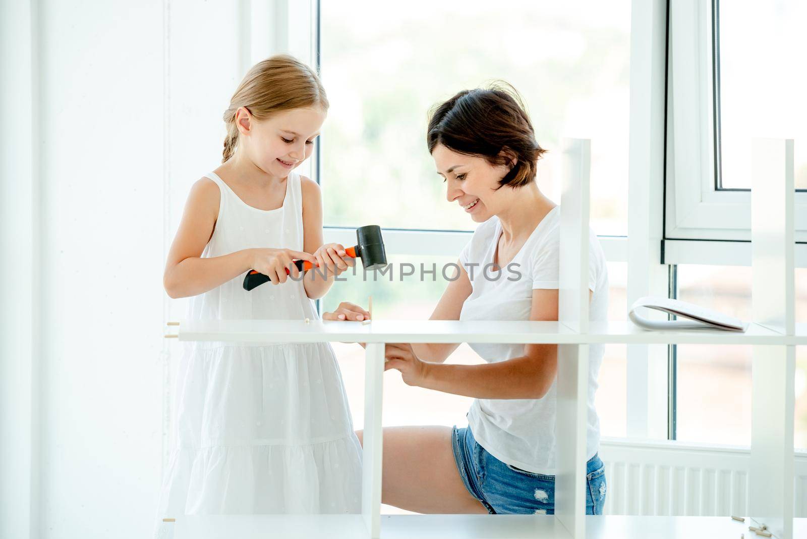 Schoolgirl teen in dress is helping mother with home labor, installing new furniture