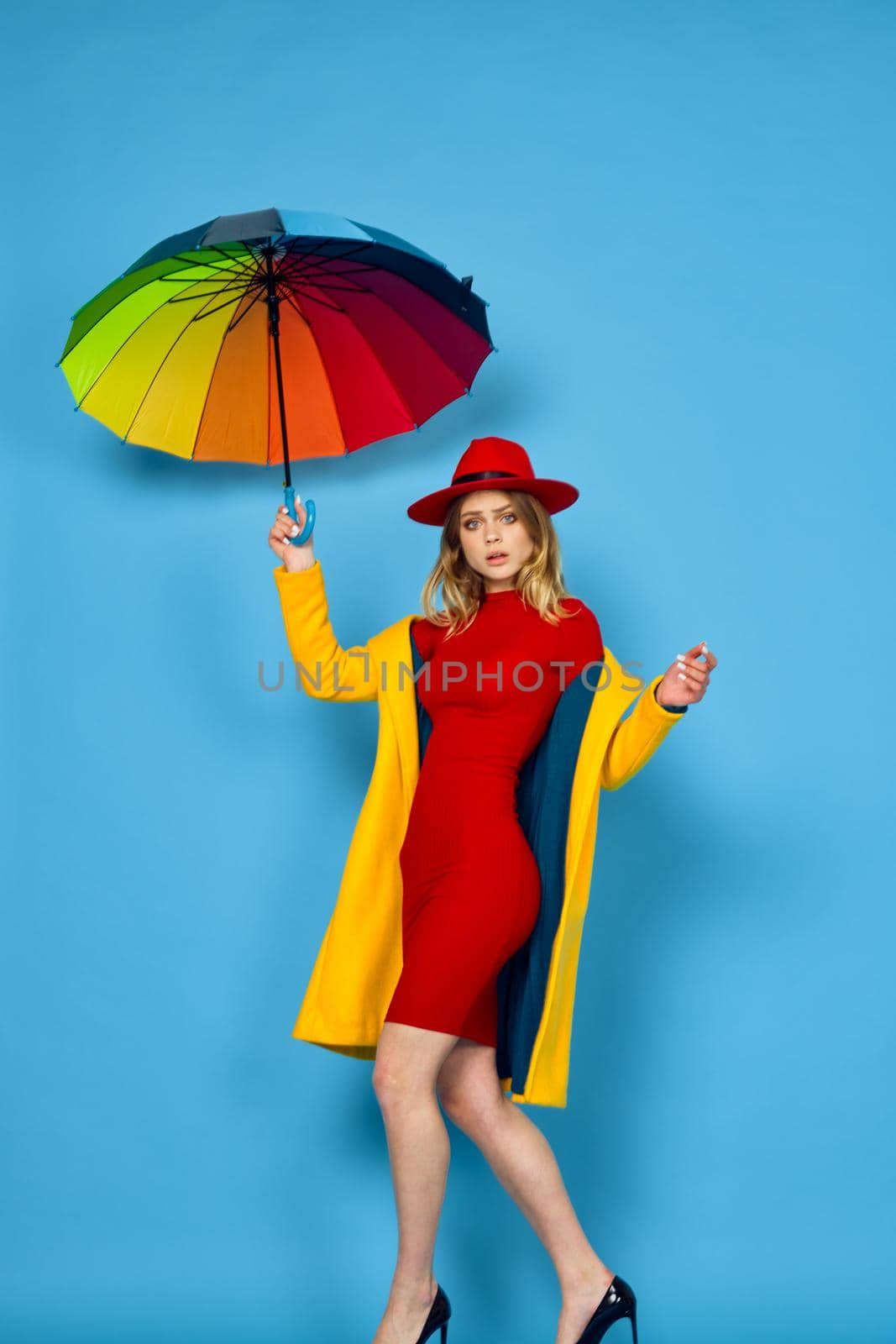 woman in yellow coat multicolored umbrella posing blue background. High quality photo