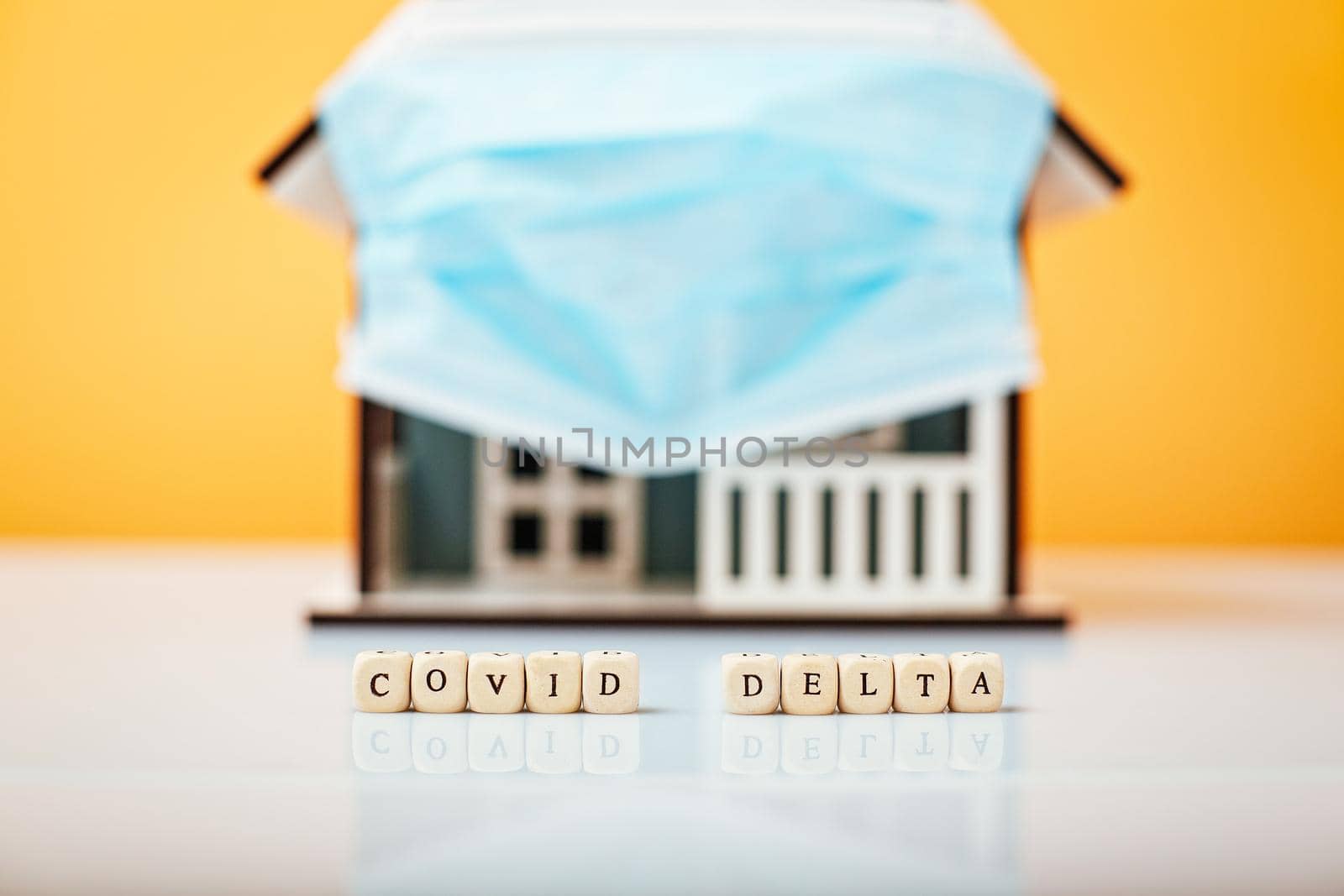 Inscription Covid Delta. Model house in a protective medical mask on a yellow background. by Maximusnd