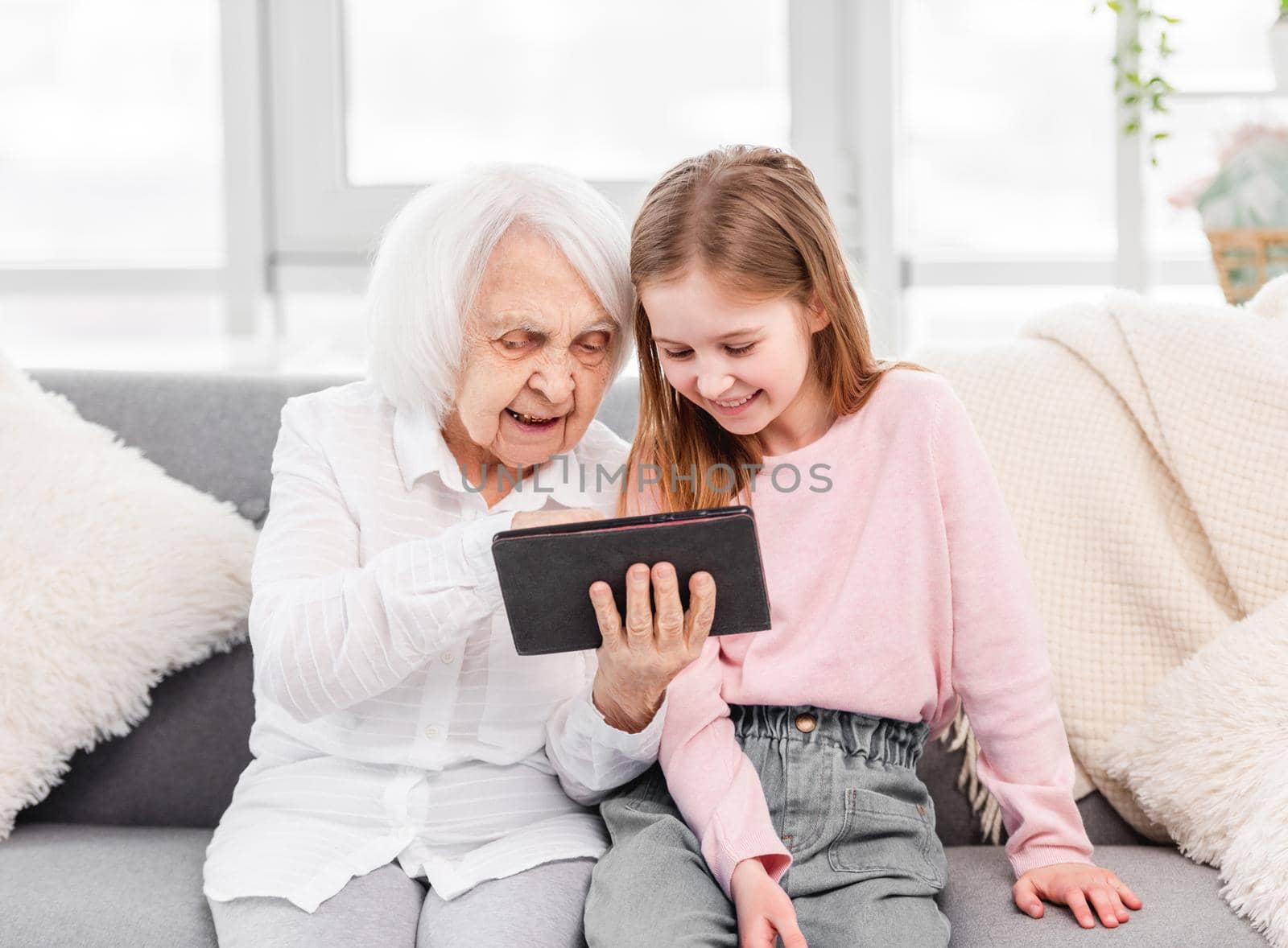 Grandmother with grandaughter looking at the tablet together and smiling at home