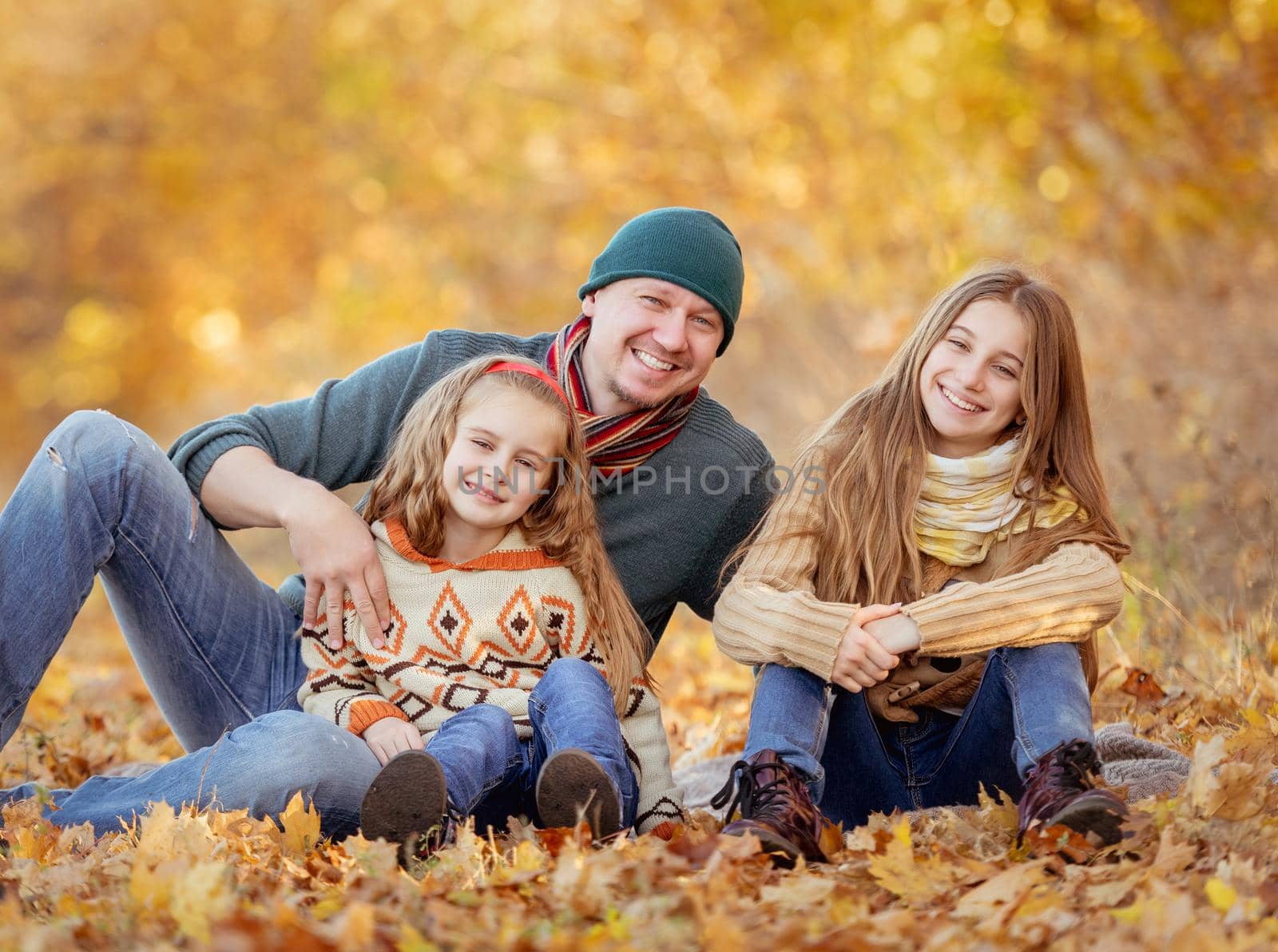 Daughters and father sitting in autumn leaves