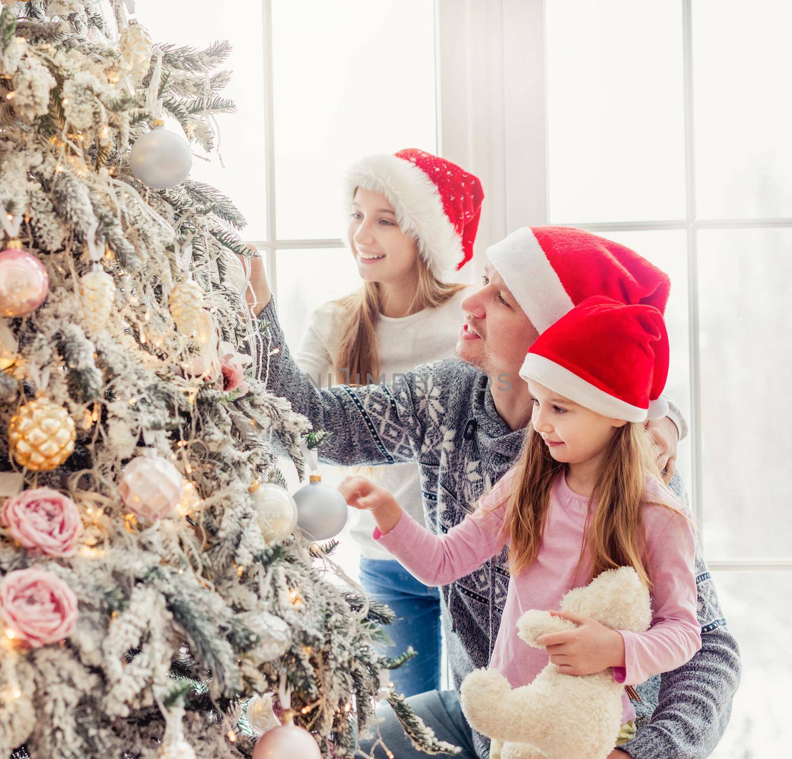 Father and daughters in santa hats decorating christmas tree
