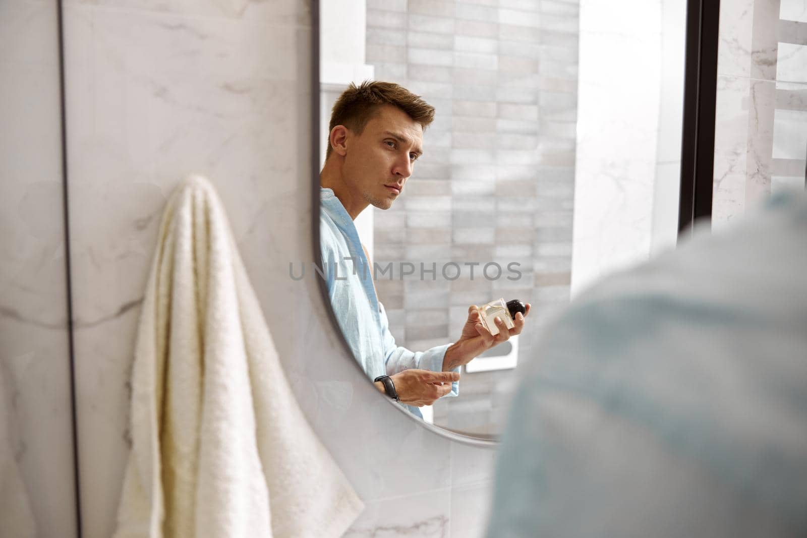 Photo of adult caucasian beautiful man in front of mirror in light modern bathroom