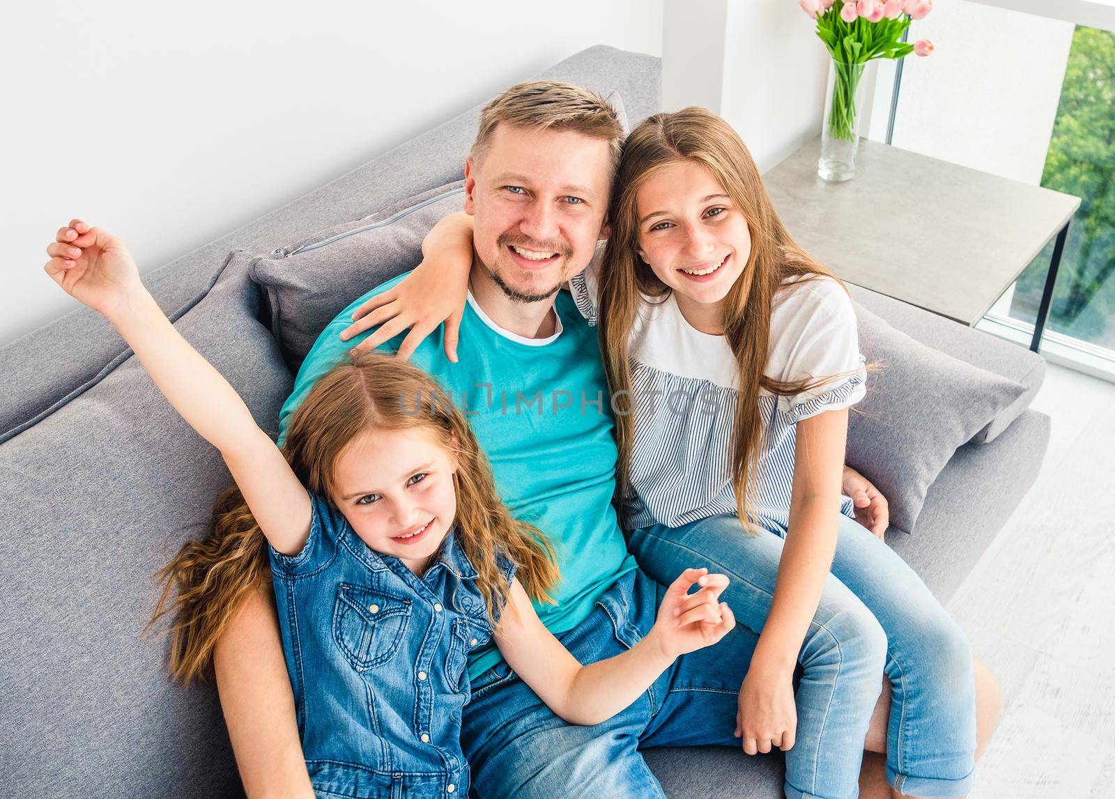 Lovely family of dad and two sisters are spending free time on the couch in the living room