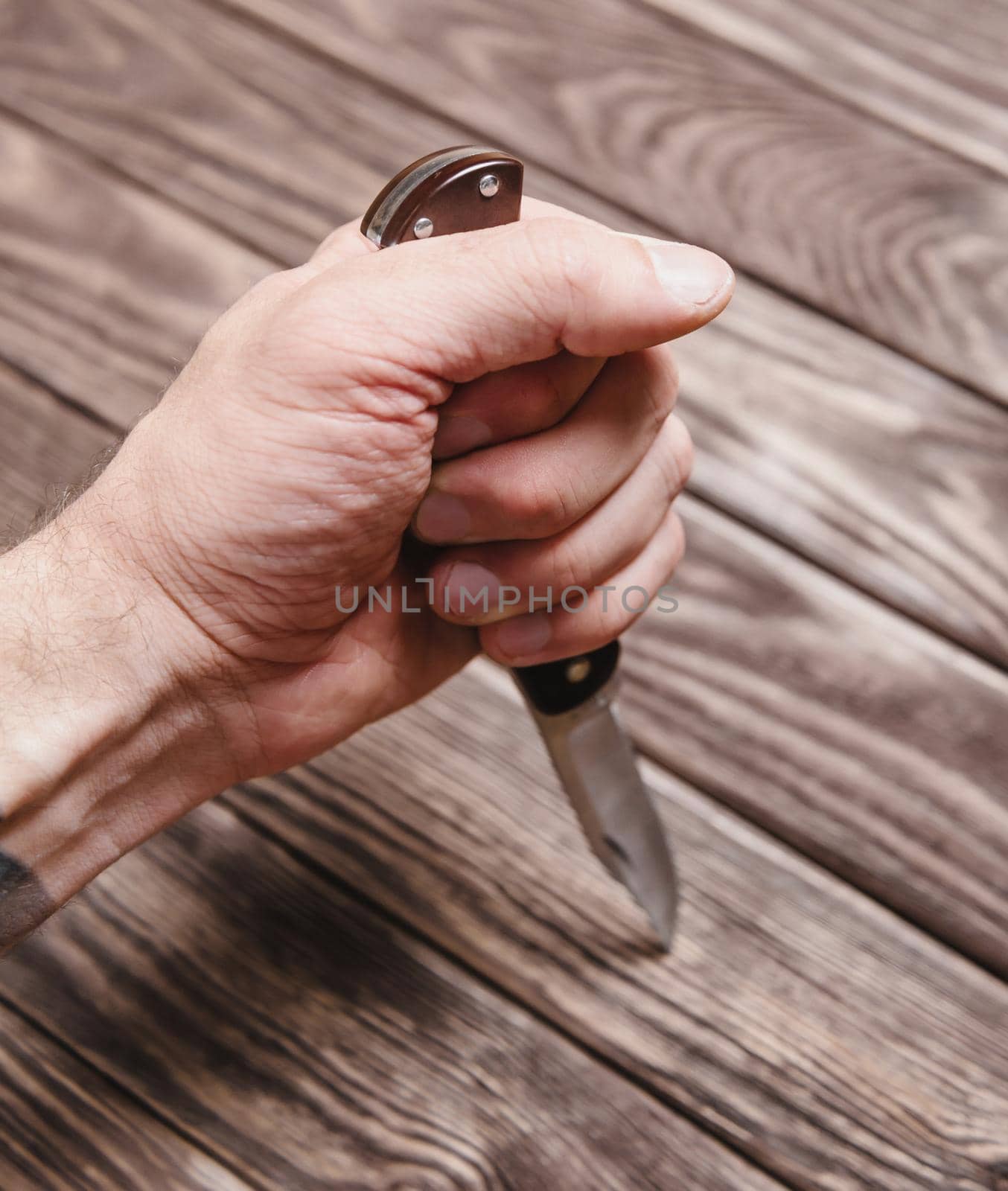 Man holding stainless jackknife on a wooden background, view of hand.