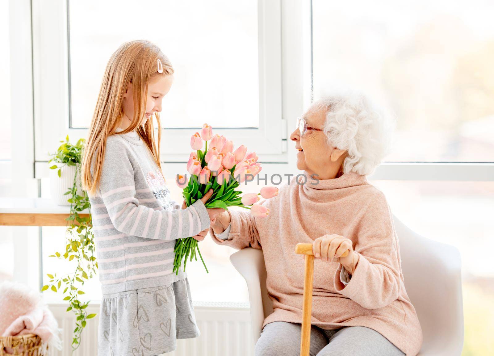 Nice little girl presenting bouquet to her grandmother in light room