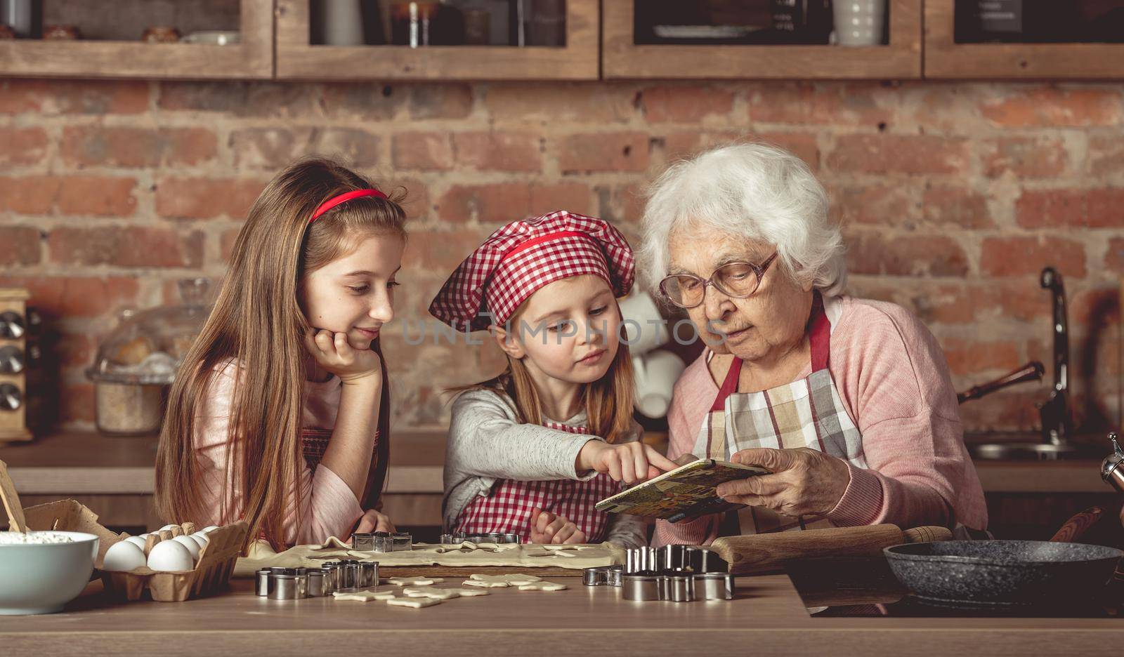Grandma and granddaughters are spreading dough using a rolling pin