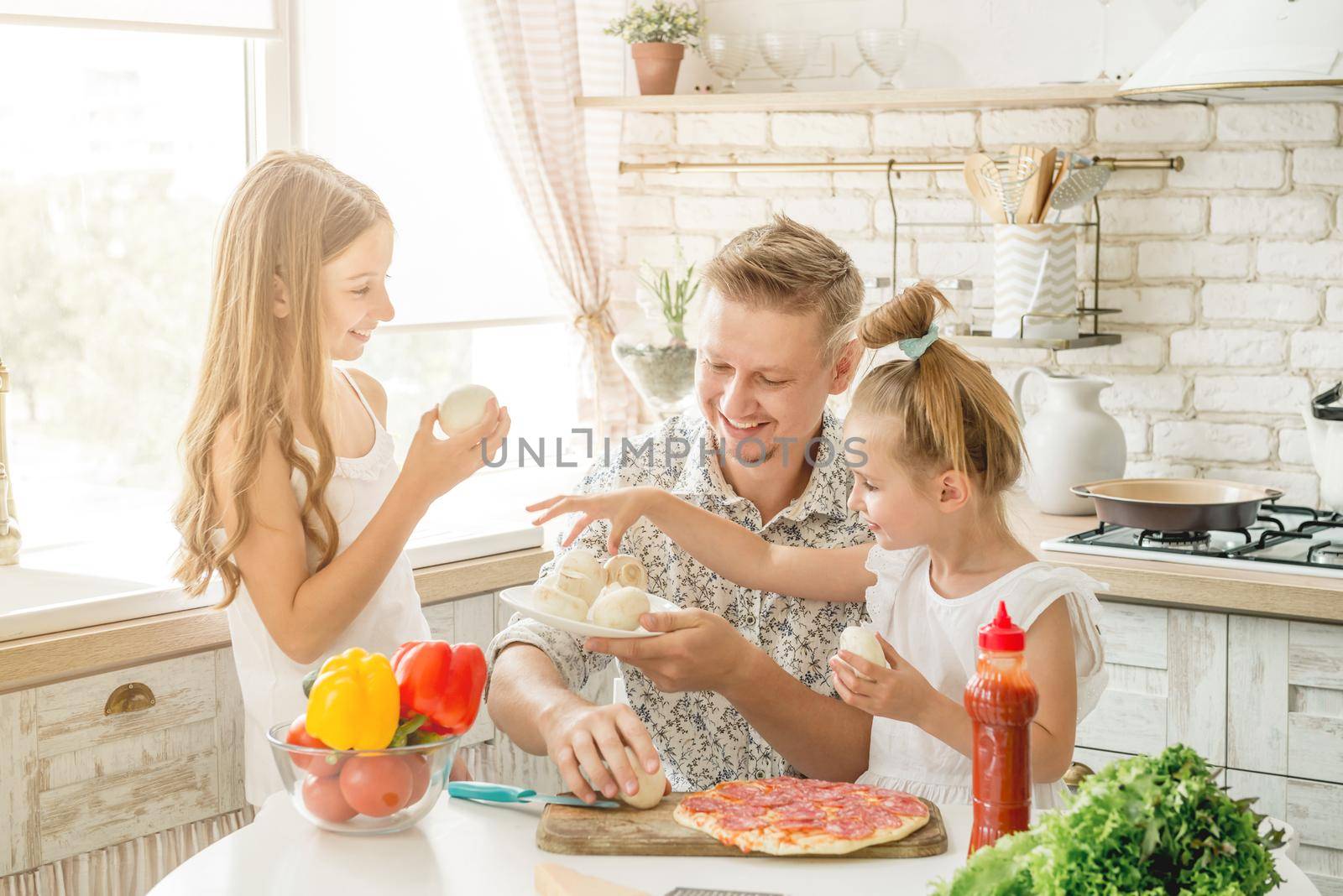 Dad with two small daughters preparing pizza with mushrooms in the kitchen