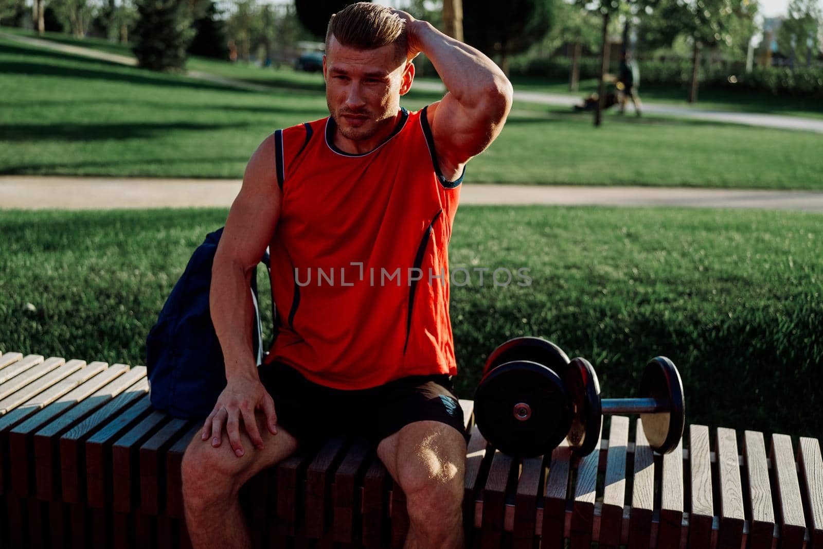 Cheerful male athlete in the park sits on a bench. High quality photo