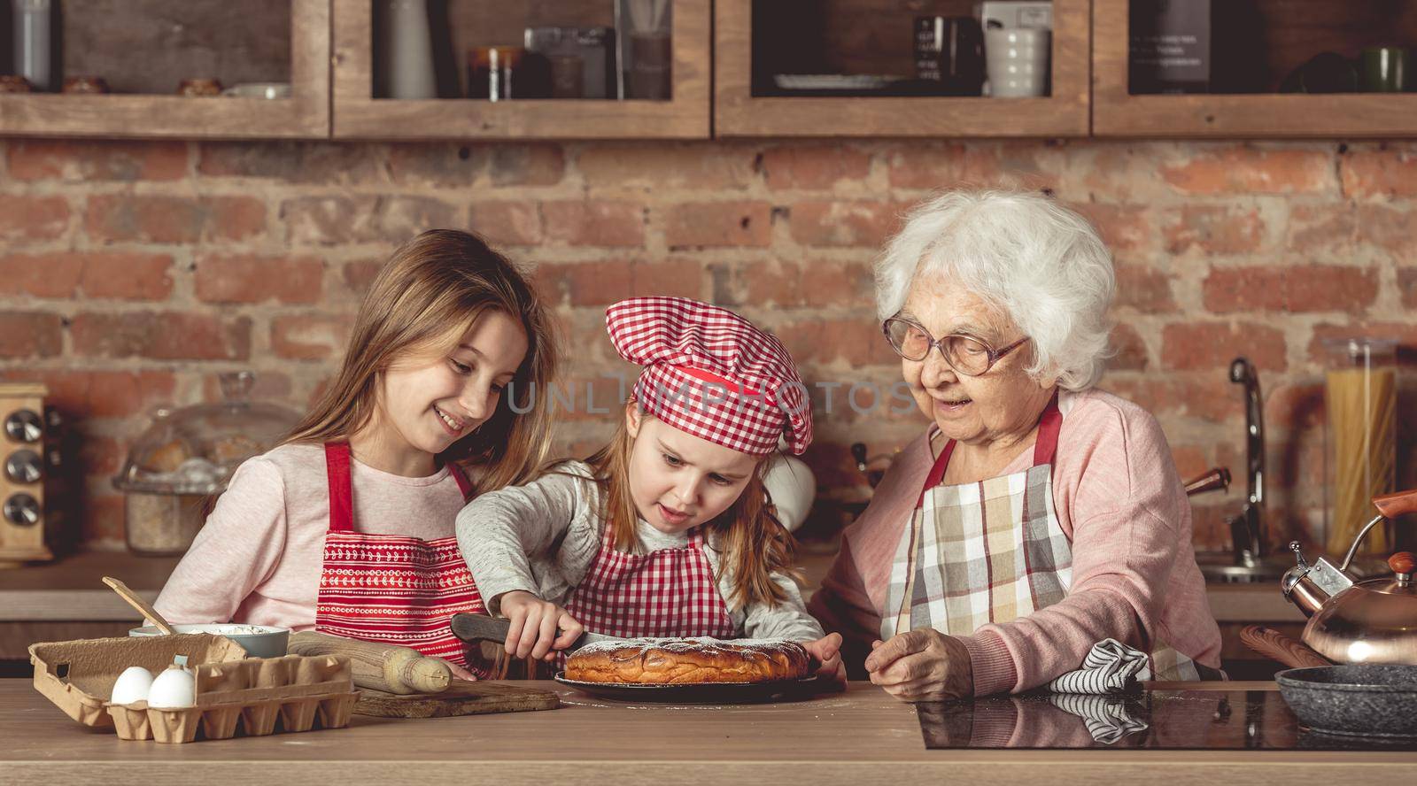 Granny with her lovely granddaughters tasting delicious homemade pie at kitchen