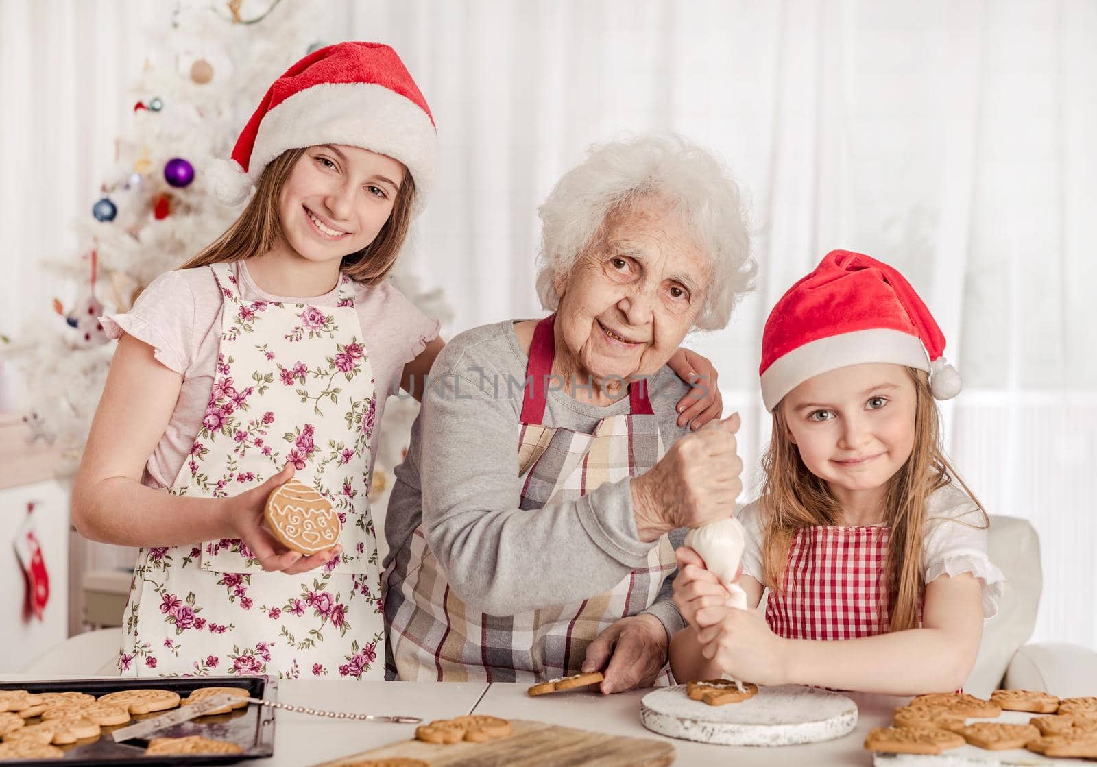 Grandmother with granddaughters in santa hats decorating cookies with cream