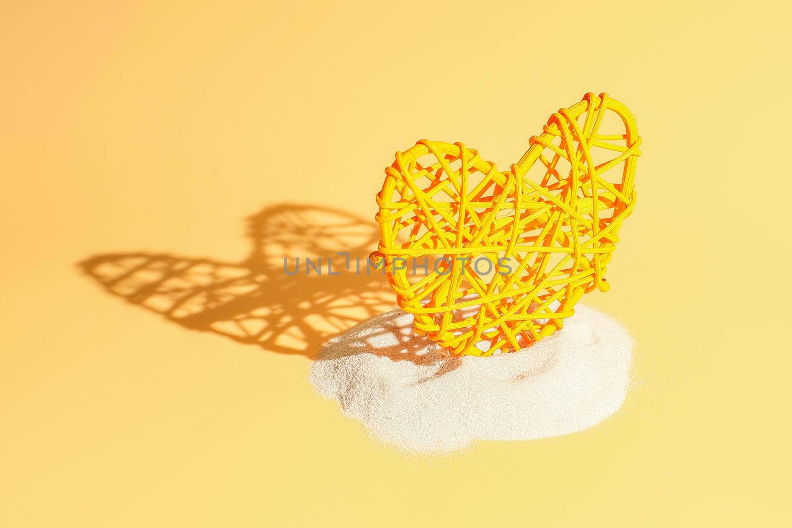 Heart in sand on yellow background, concept with shadow