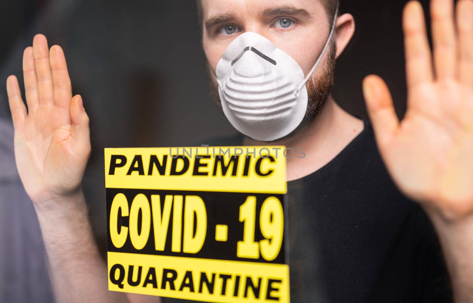 Coronavirus, quarantine and pandemic concept. Sad and sick man of corona virus looking through the window