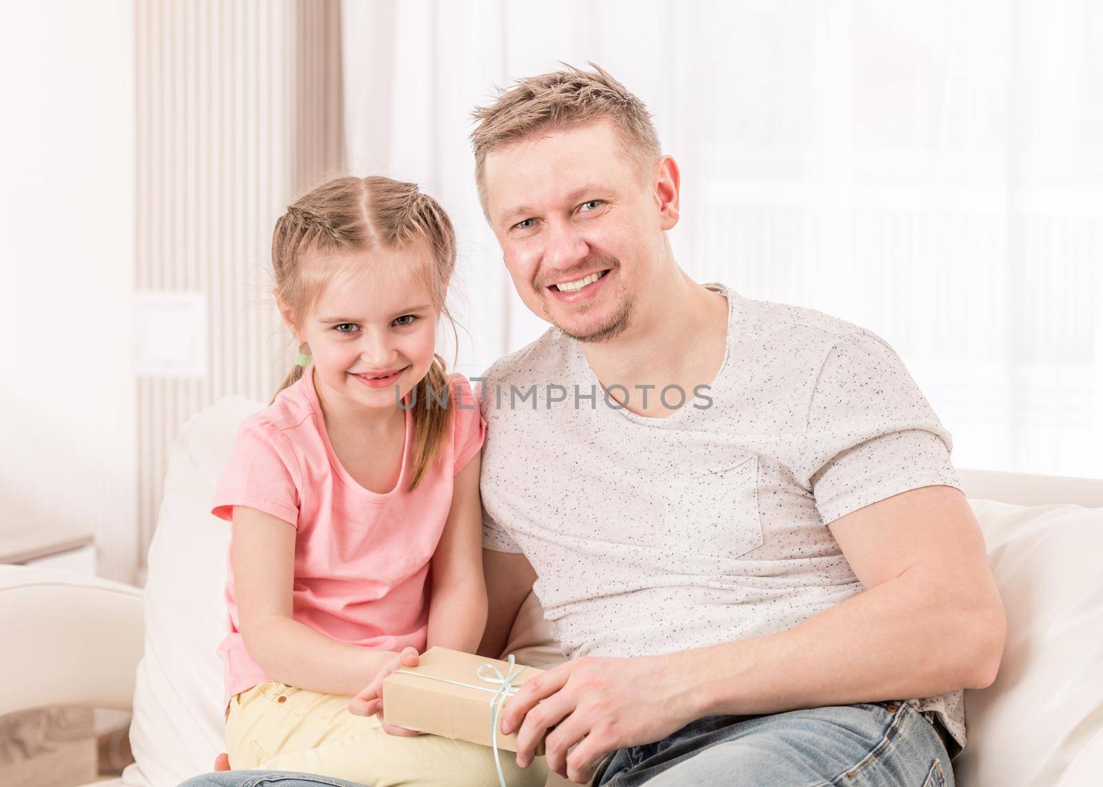 Dad with daughter opening Fathers day gift on sofa by tan4ikk1