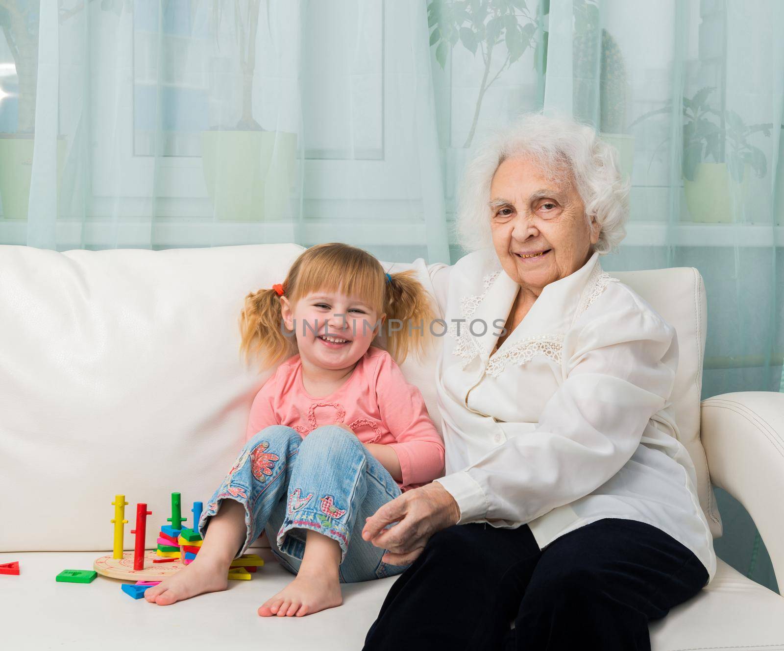 little girl with grandmother sitting on a sofa with toys