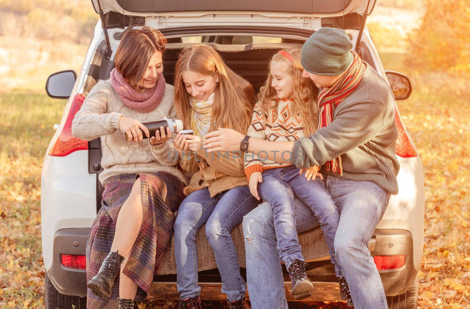 Happy family sitting in car trunk on autumn background