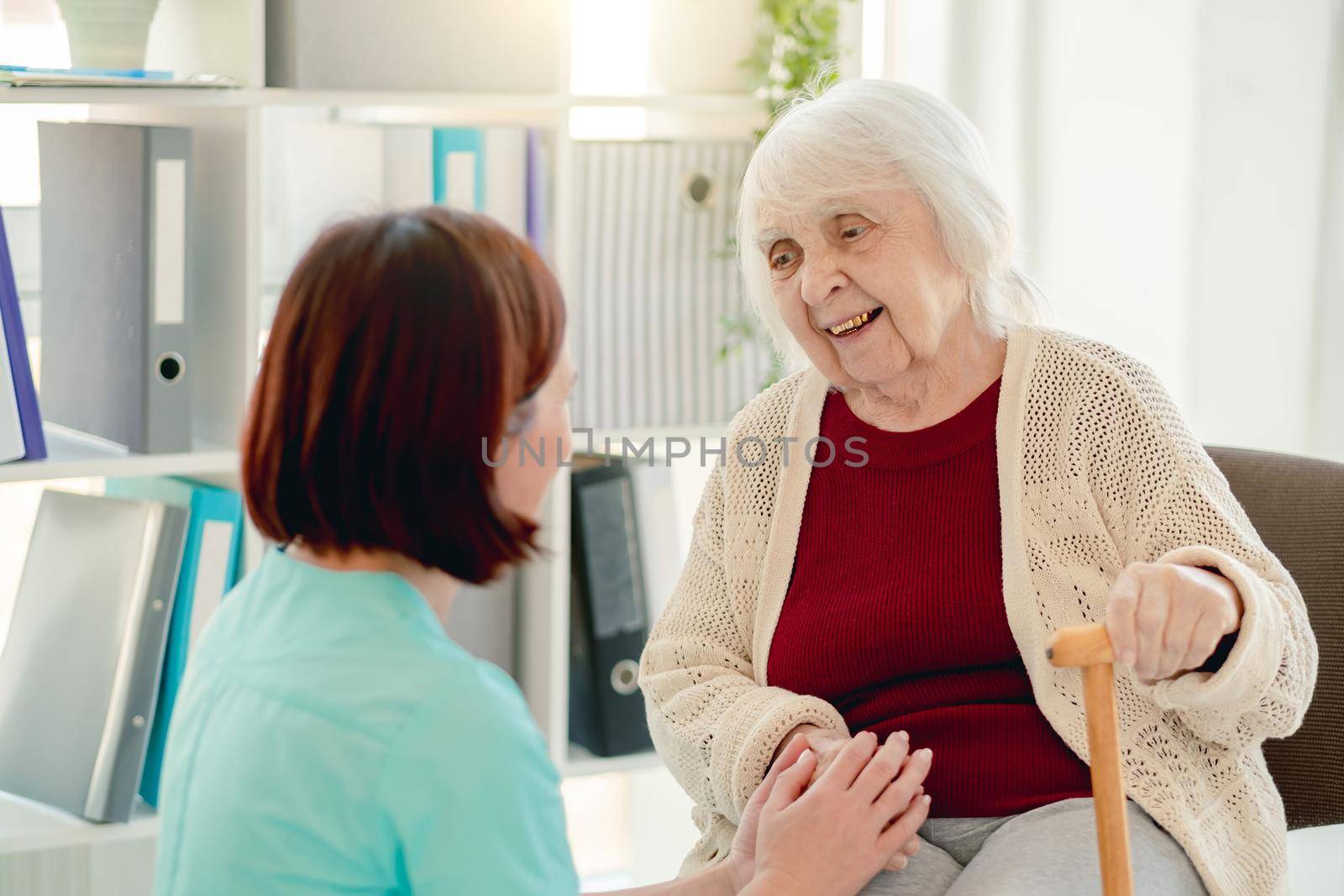 Old lady talking to caregiver holding hands in nursing home