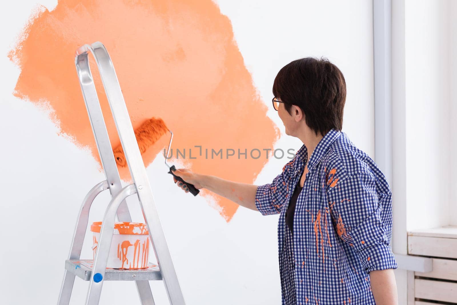 Renovation, redecoration and repair concept - middle-aged woman painting wall in new apartment.