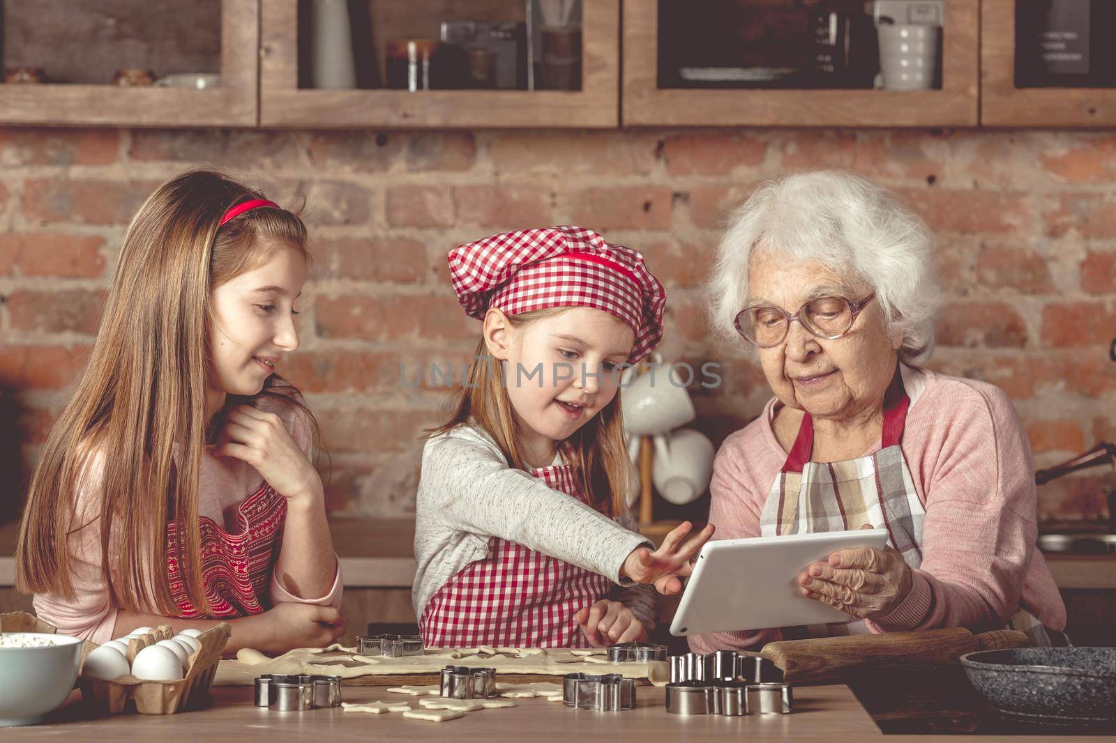 Grandma with granddaughters looking for a recipe in tablet by tan4ikk1