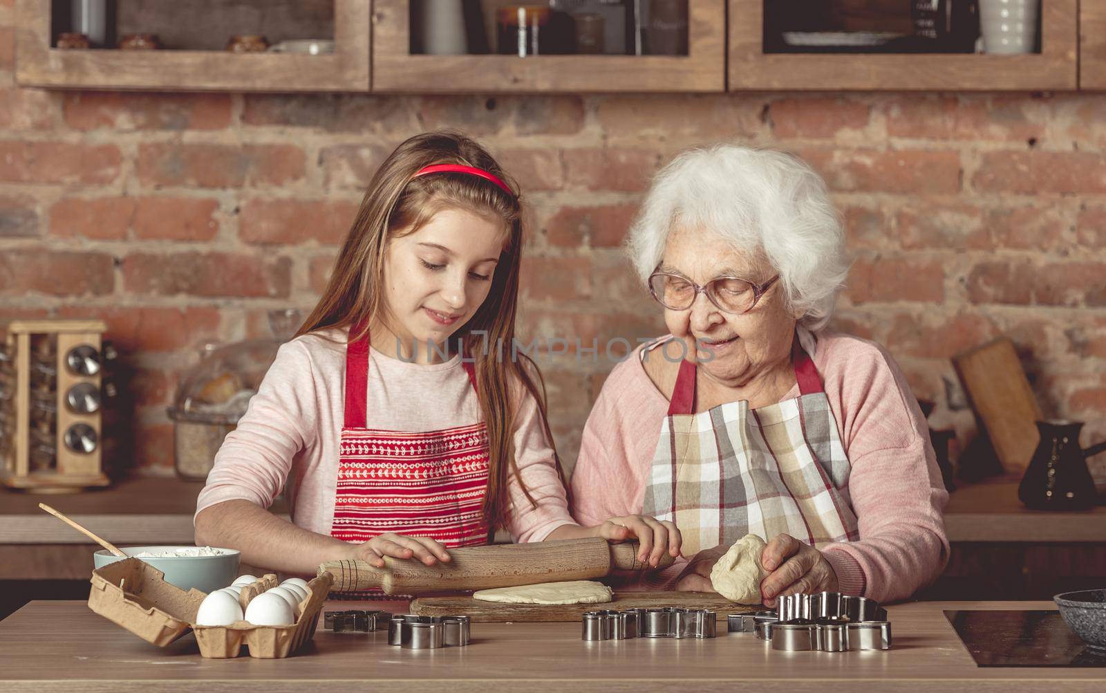 Elderly woman teaching a little girl to bake cookies by tan4ikk1