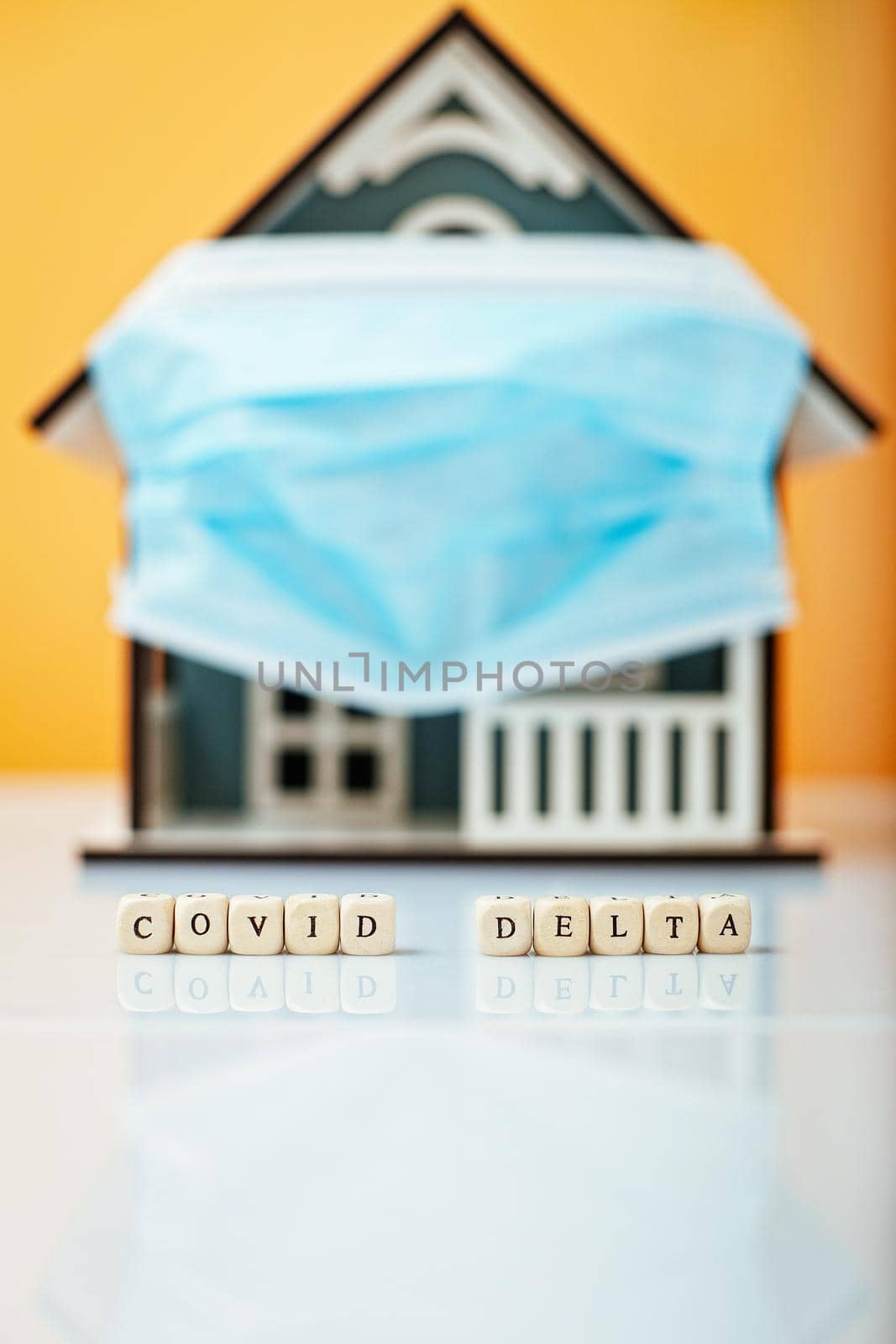 Inscription Covid Delta. Model house in a protective medical mask on a yellow background.