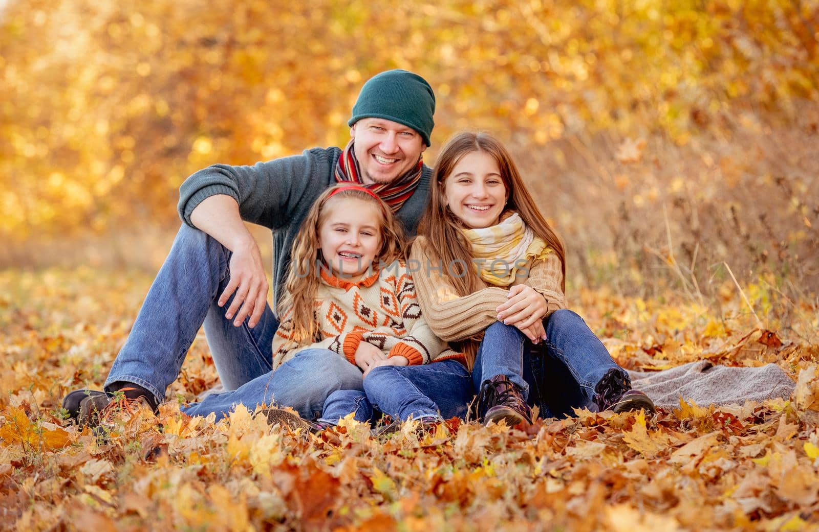 Daughters and father sitting in autumn leaves