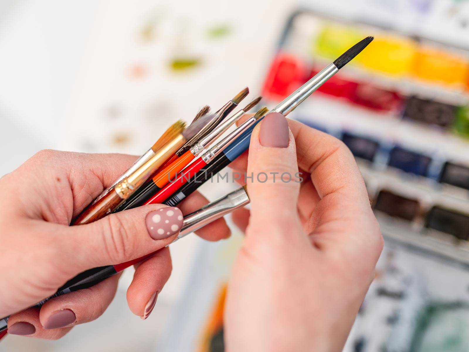 Artist hands with different size and colors paintbrushes closeup view with watercolor on background