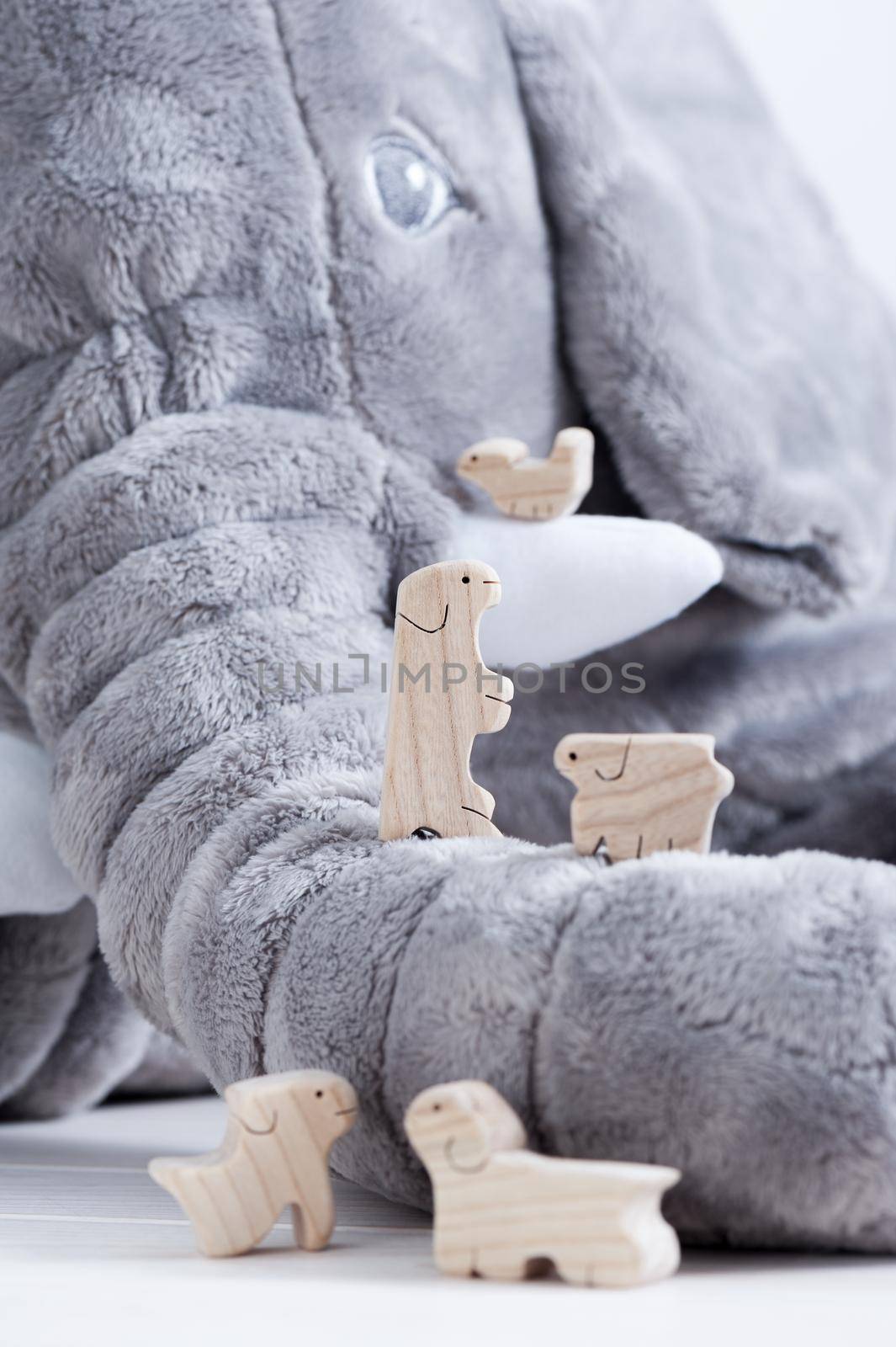 cute wooden toy animals on white wood plank with giant elephant doll in the background, tiny toys and shallow depth of field