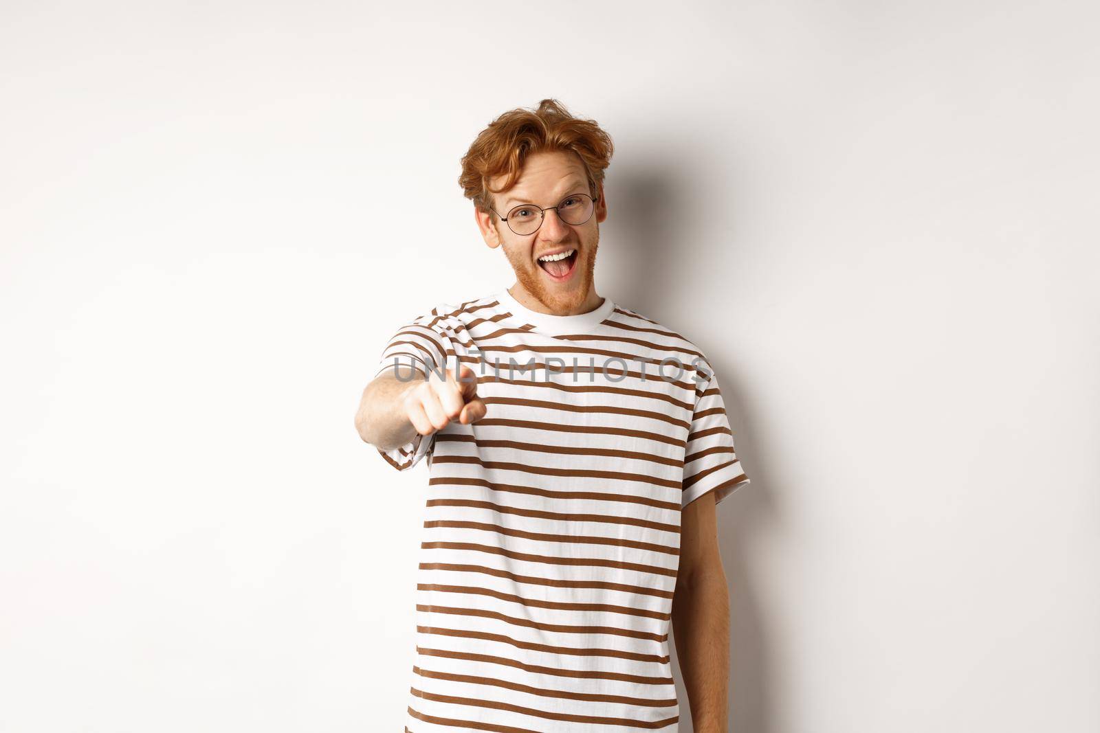 Image of funny redhead guy in glasses laughing at you, pointing finger camera and making fun of someone, standing over white background.