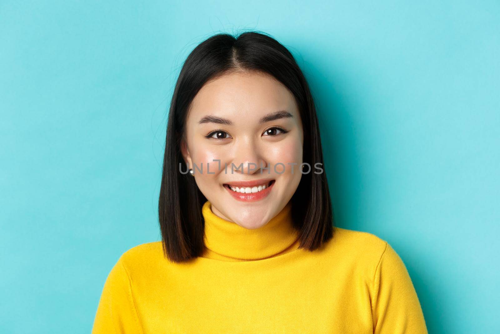 Beauty and skincare concept. Close up of smiling asian female model with perfect skin and white teeth, standing over blue background.