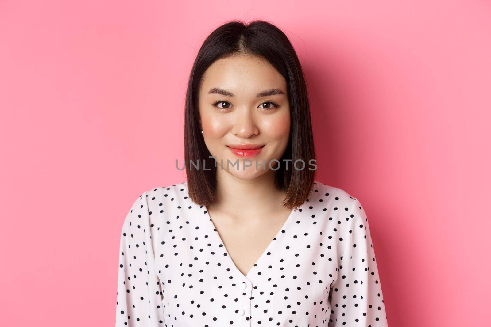 Close-up of cute asian female model looking at camera, blushing and smiling kawaii, standing over pink background by Benzoix