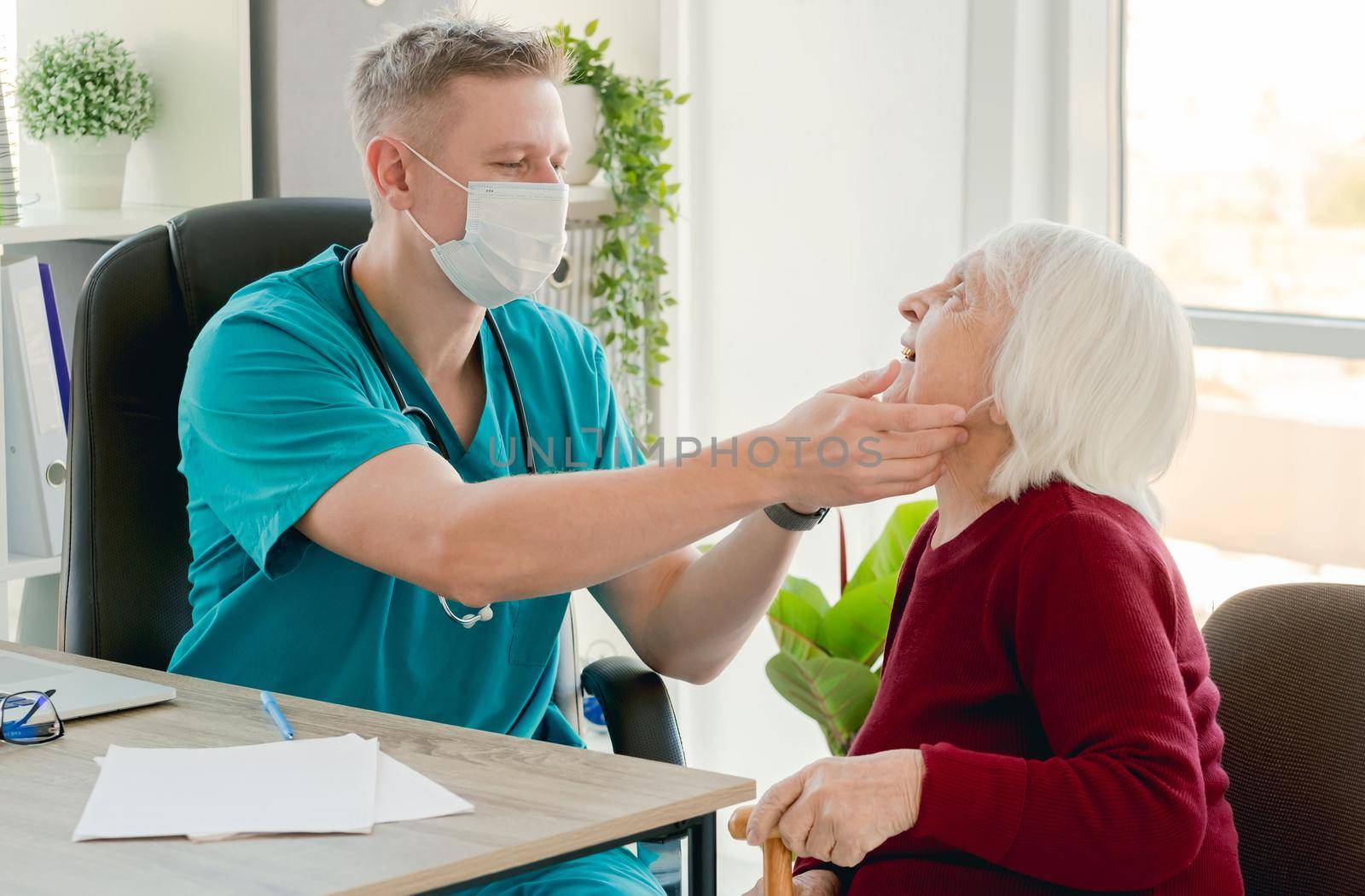 Doctor examining throat of old woman by tan4ikk1