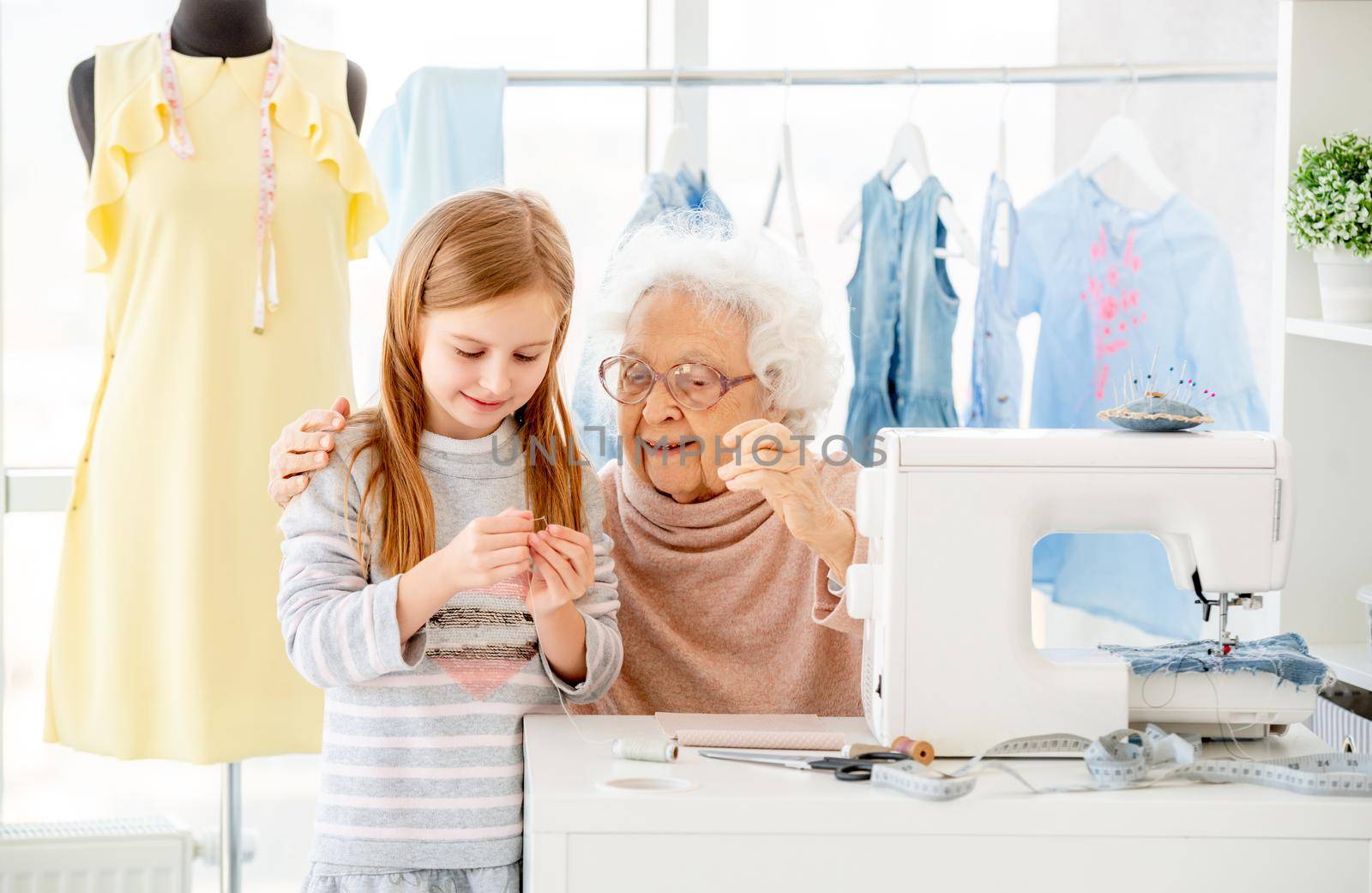 Senior woman instructing little girl how to thread needle