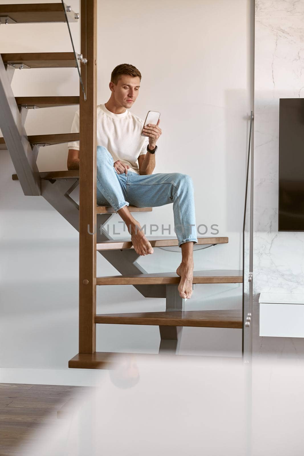 Relaxing happy caucasian man on the minimalistic stairs in modern light apartment by Yaroslav_astakhov