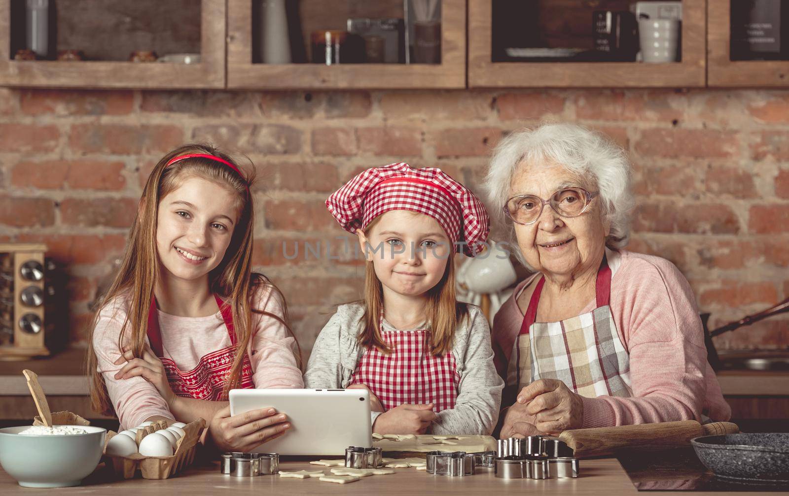 Grandma with her little granddaughters looking for a recipe using modern tablet