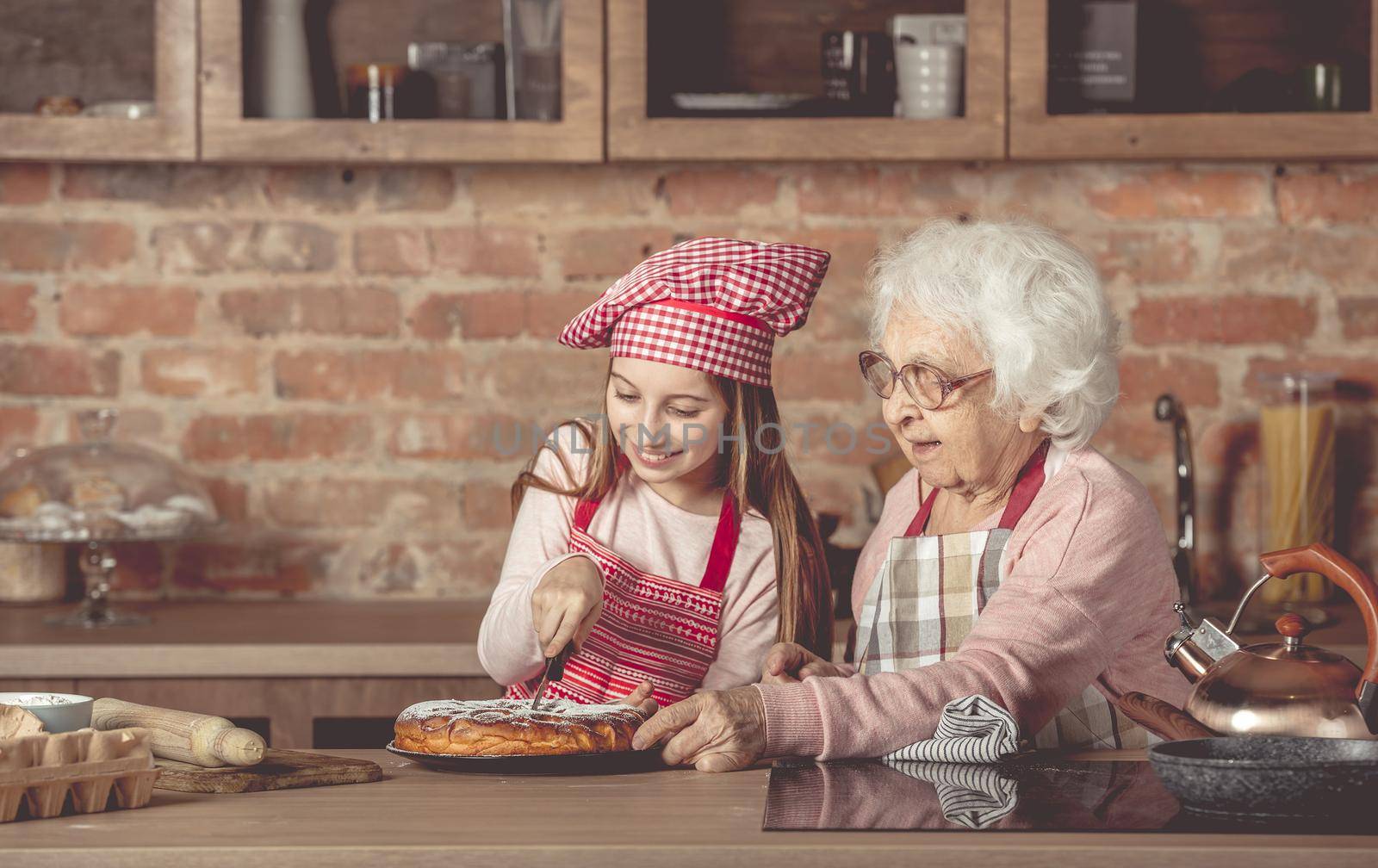 Granddaughter with her grandmother sitting at the kitchen and cut the homemade pie