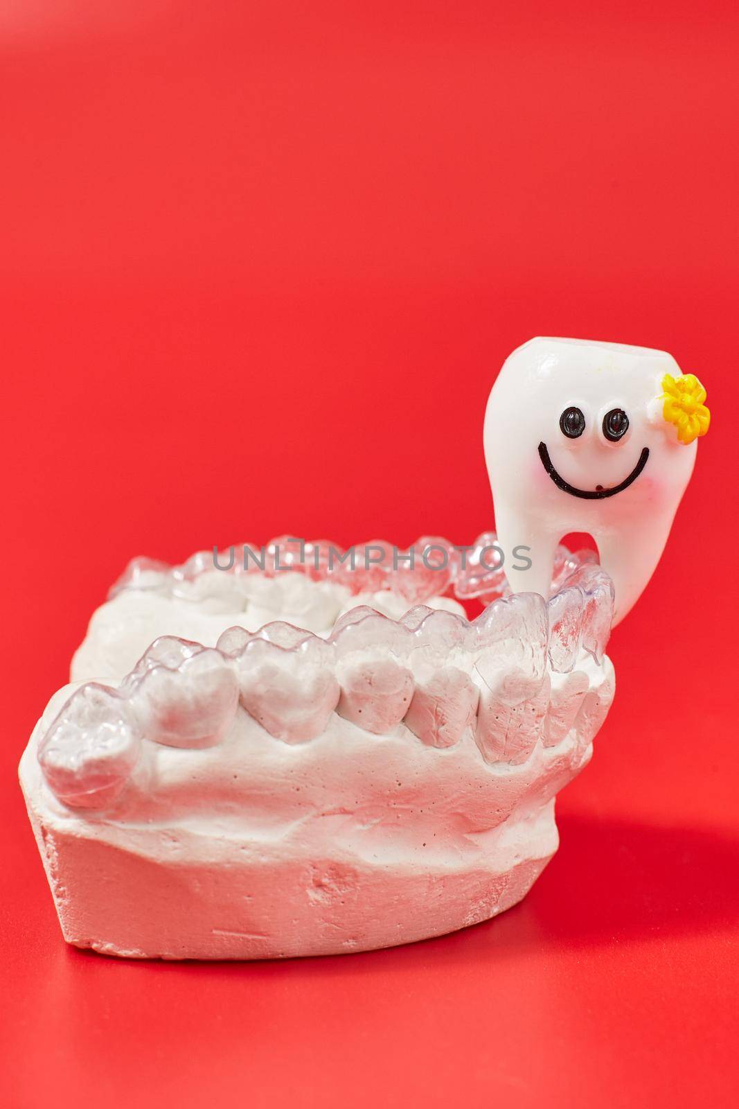 Joyful tooth on a red background in invisible dental aligners or braces aplicable for an orthodontic dental treatment by Maximusnd