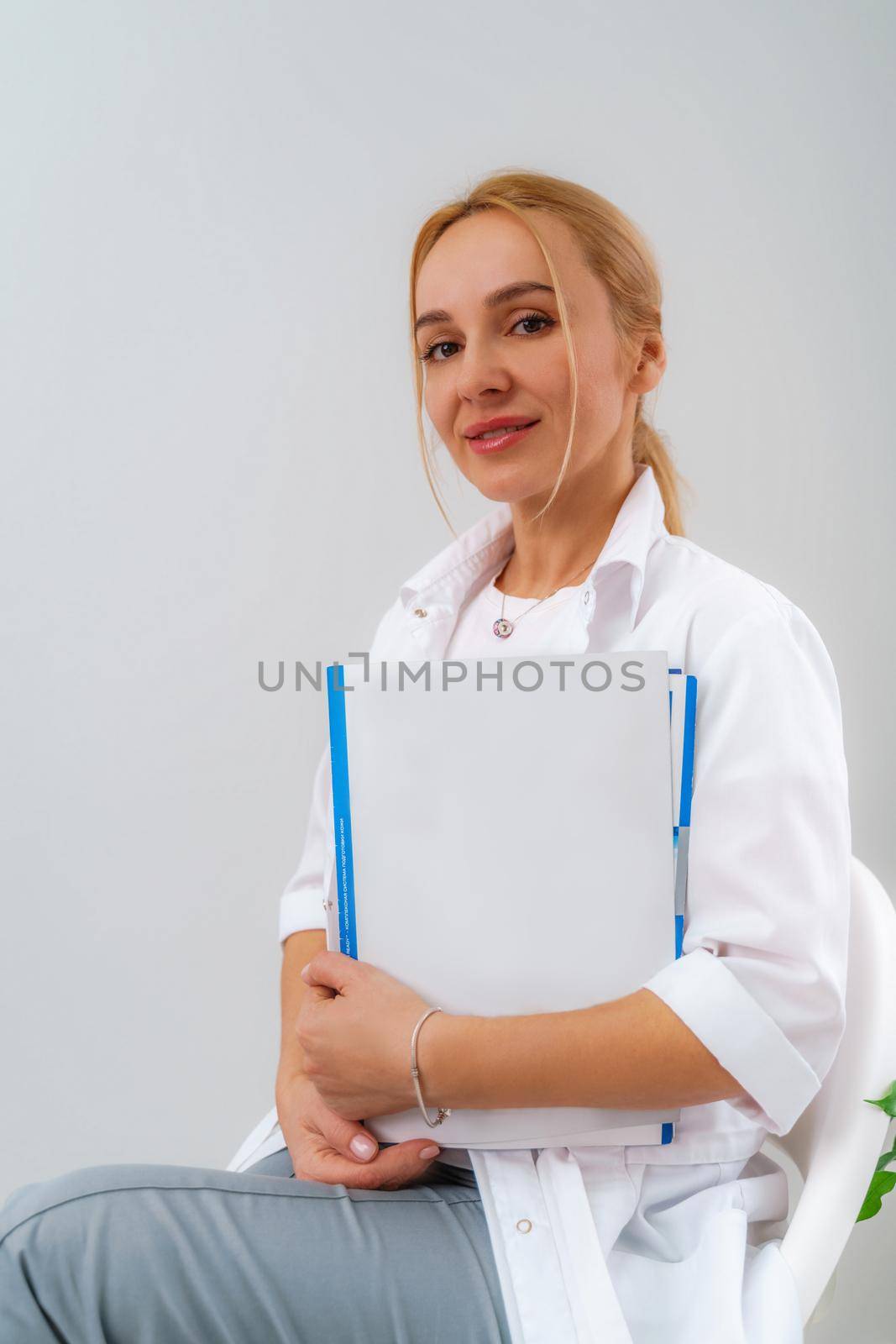 Woman doctor wear white medical uniform with blue folder of documents in clinic by Matiunina