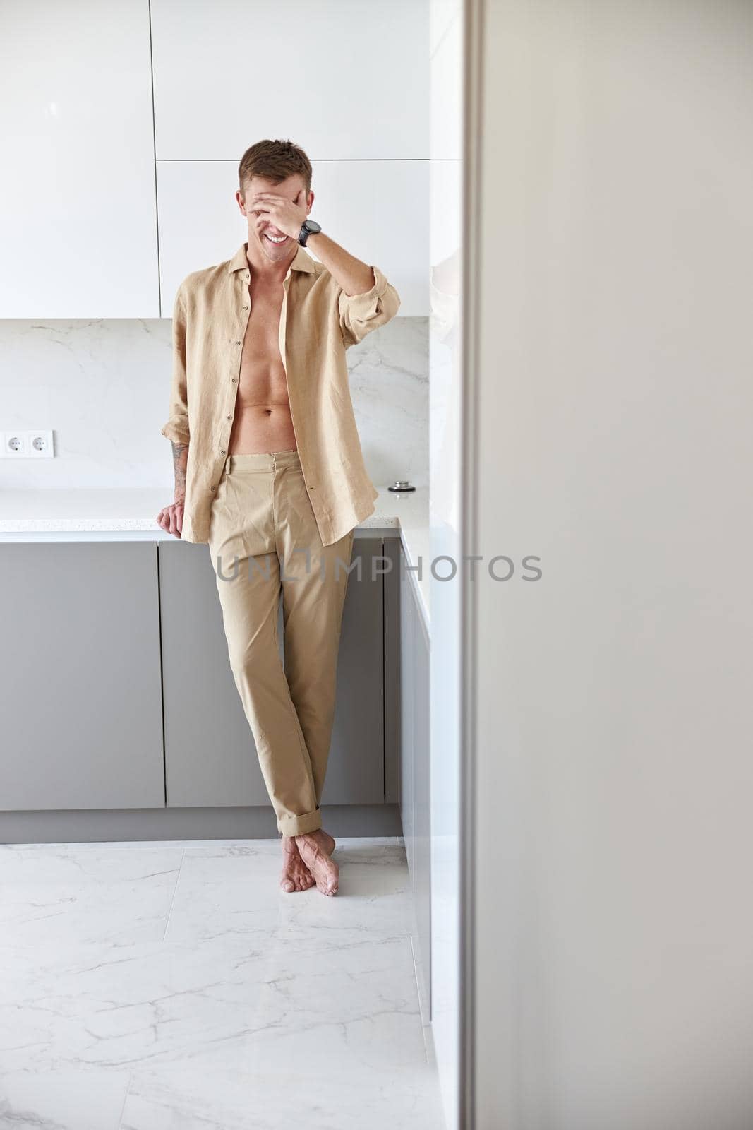 Happy handsome man is standing on minimalistic kitchen and smiling