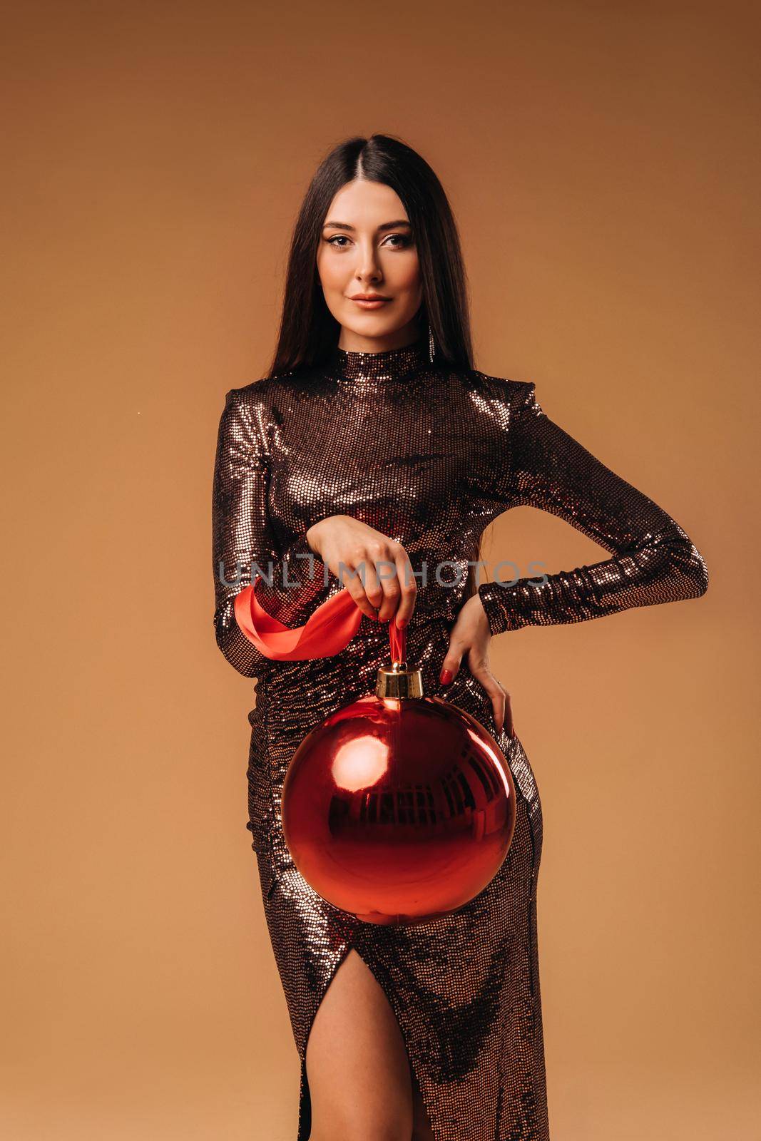 Girl with long hair in a shiny dress with a large Christmas ball on a brown background.