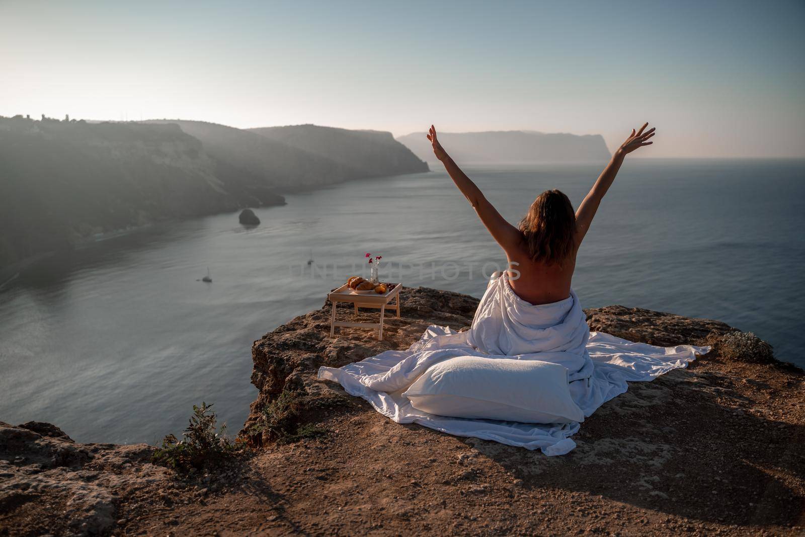 Woman wearing pajamas wake up in bed wuth duvet and pillow over nature sea background outdoors. Back view. Good morning. Freedom concept