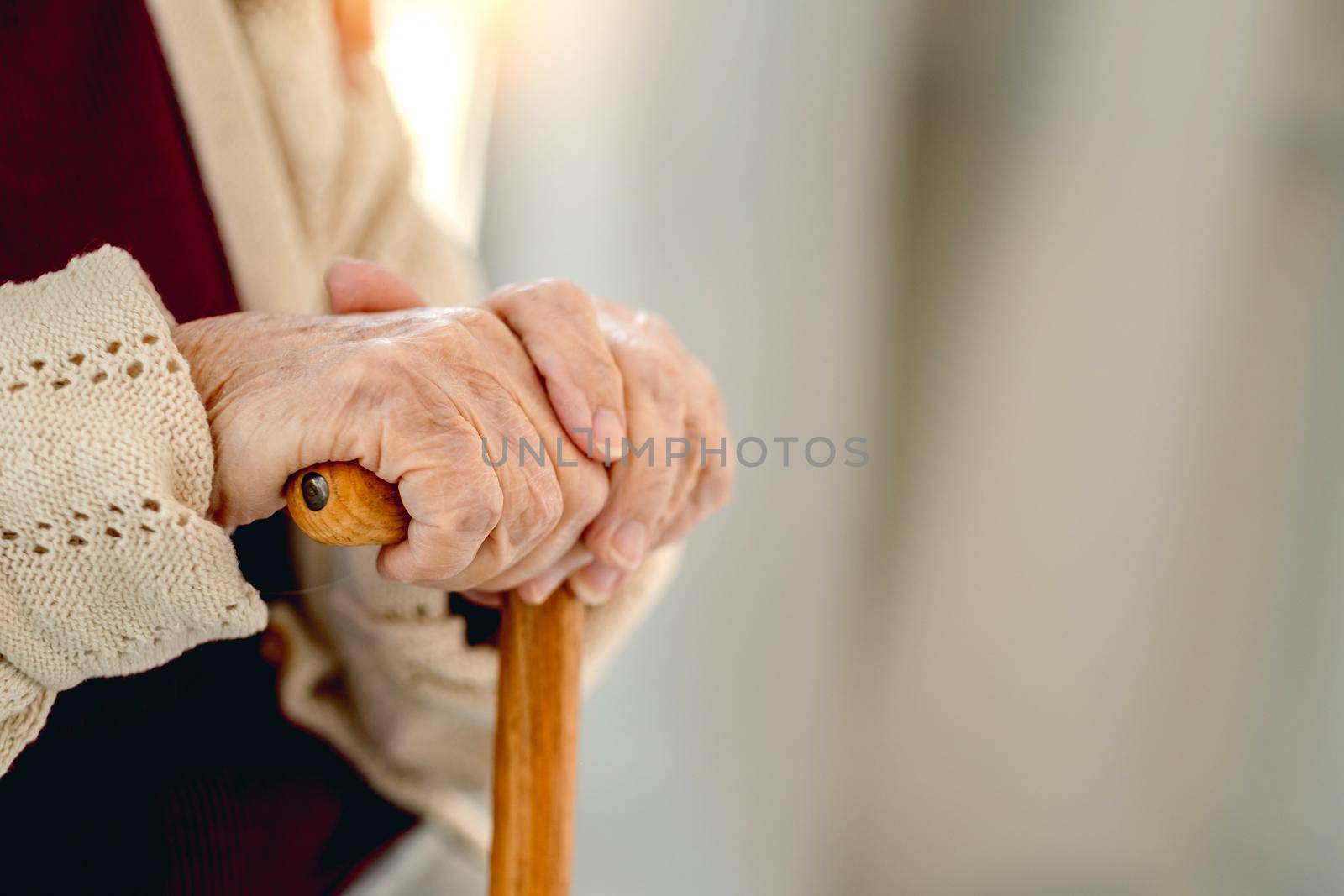 Wooden cane in hand of old woman sitting in light room