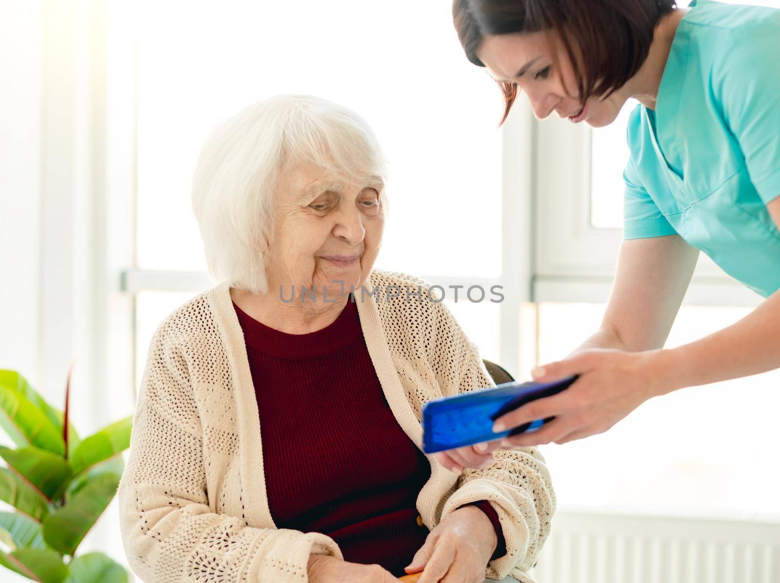 Caregiver showing phone screen to old woman patient in nursing home