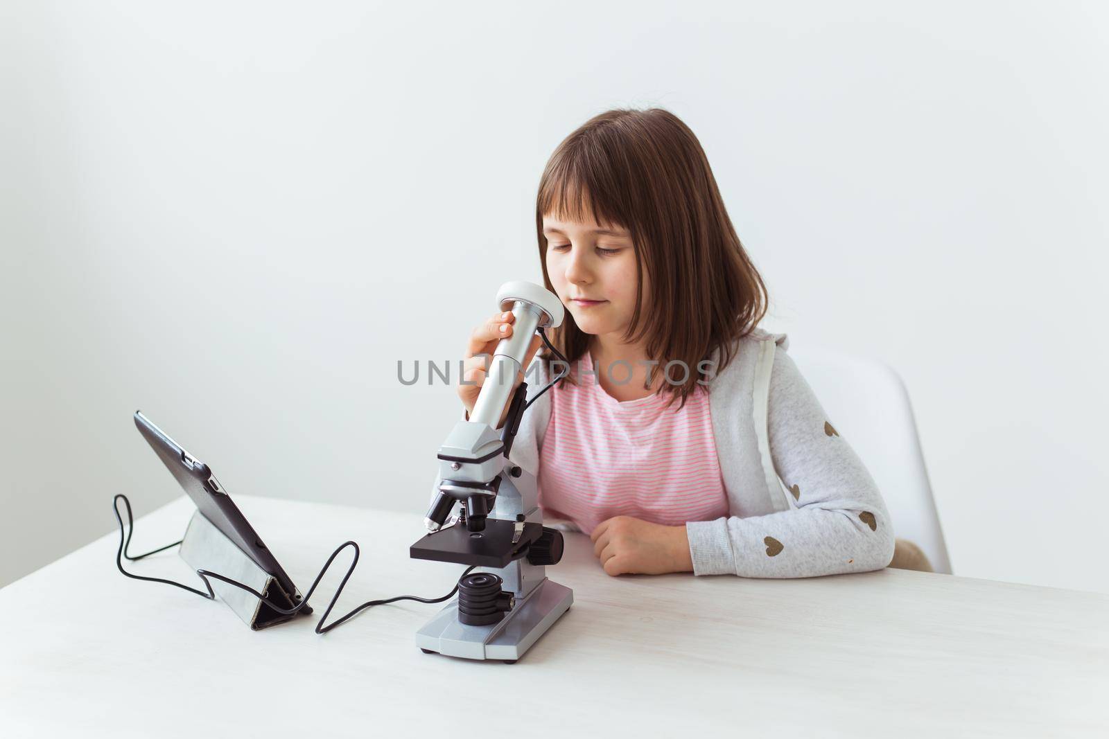 Schoolgirl using microscope in science class. Technologies, lessons and children concept. by Satura86