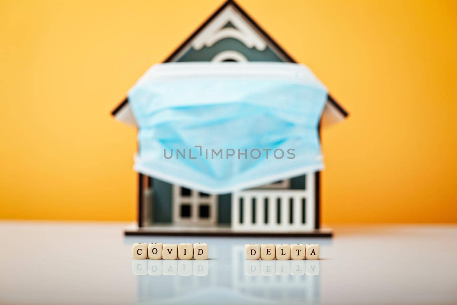 Inscription Covid Delta. Model house in a protective medical mask on a yellow background.